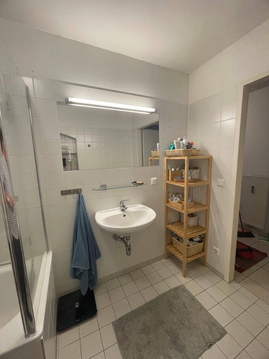 Helles Badezimmer mit Waschbecken, großem Spiegel und praktischem Holzregal für Utensilien.