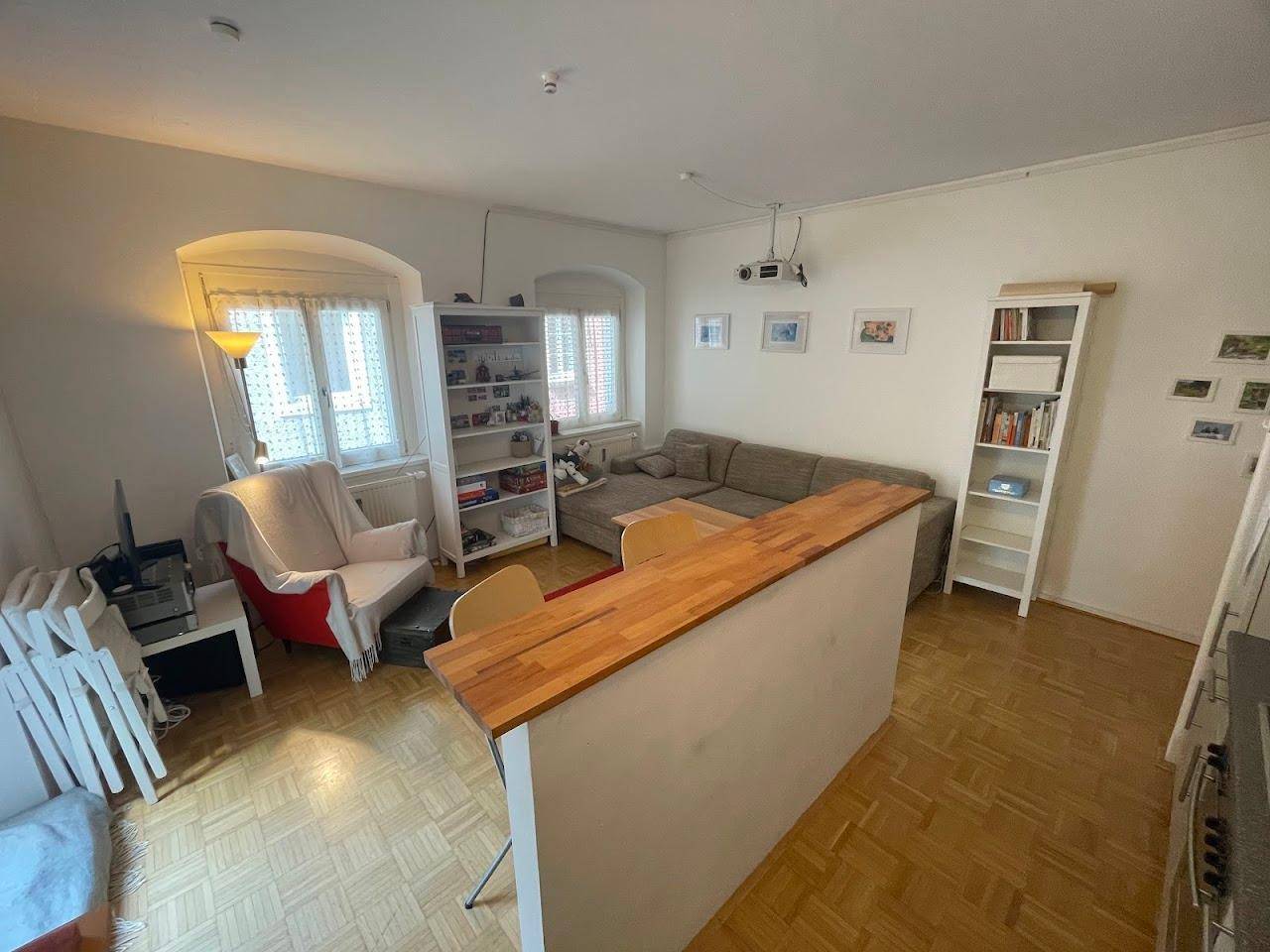 Heller Wohnbereich mit beigem Sofa, Bücherregalen und einer Holztheke, die den Raum strukturiert.