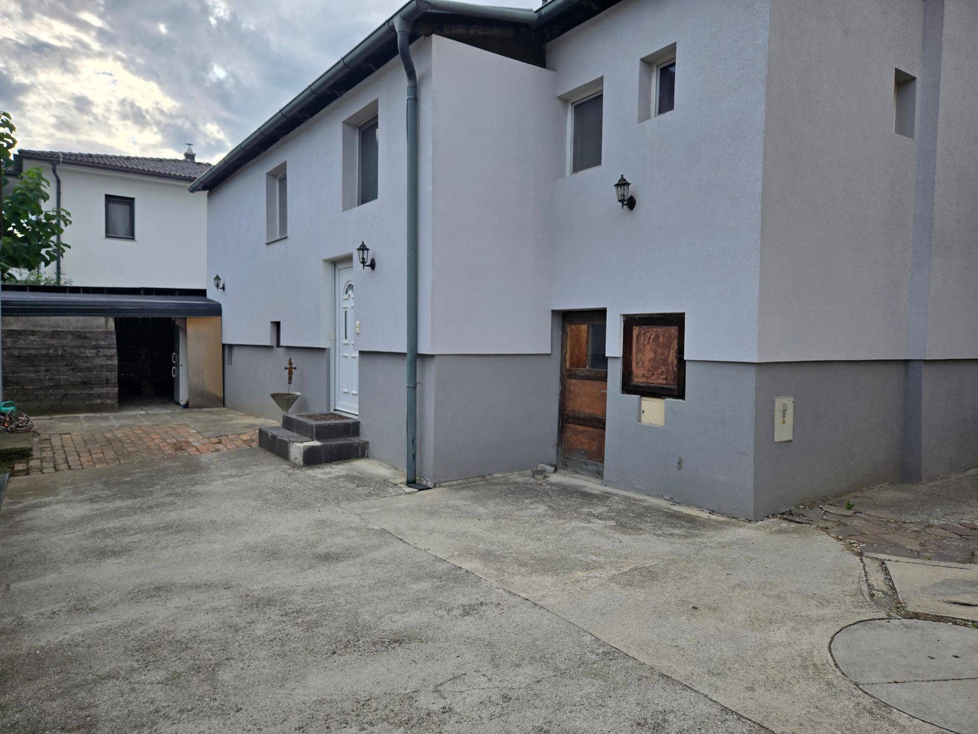 Eingangsbereich eines Hauses mit gepflasterter Auffahrt und grauer Fassade.