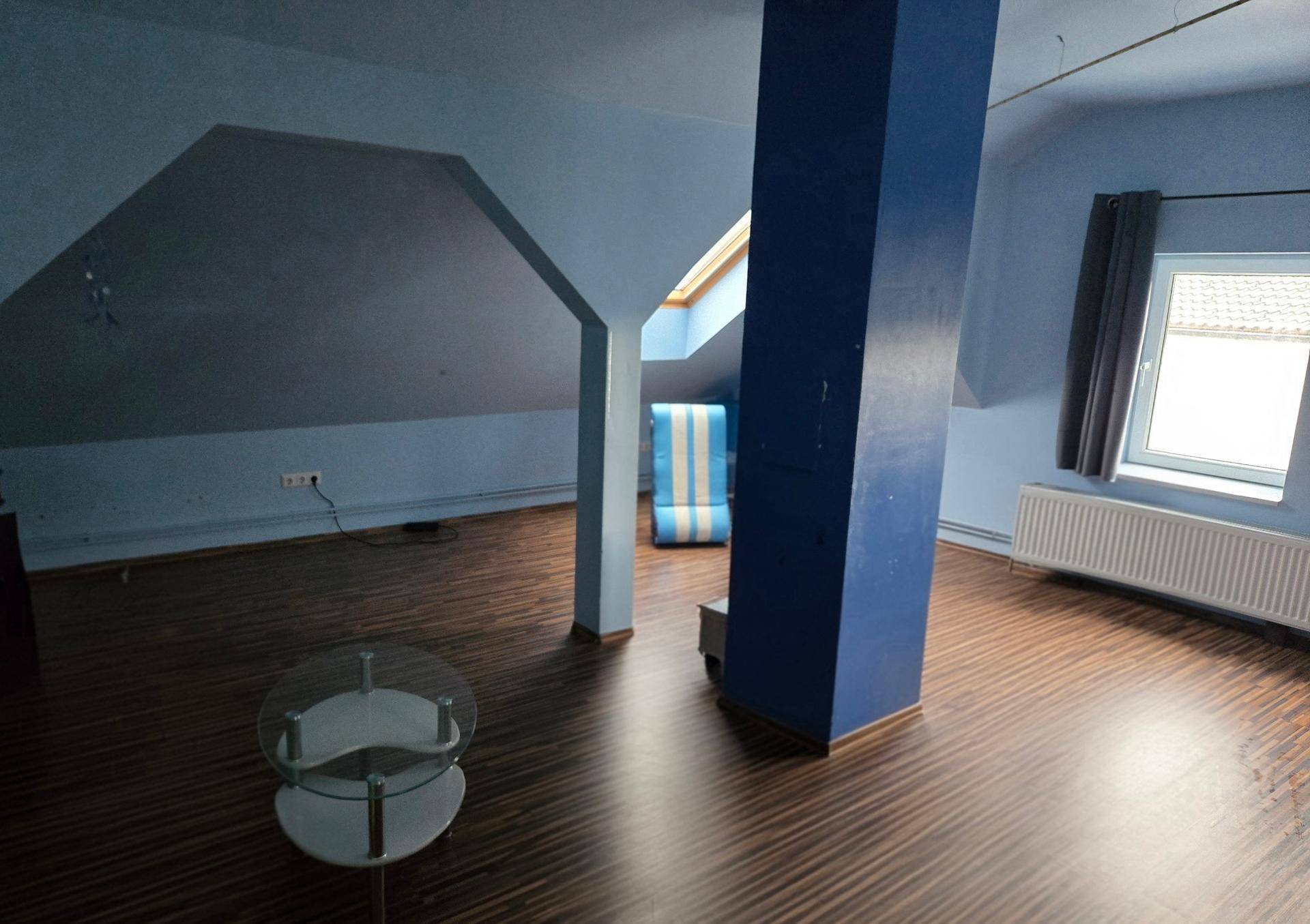Dachzimmer mit blauen Wänden, Holzboden, Säule und Dachfenster.