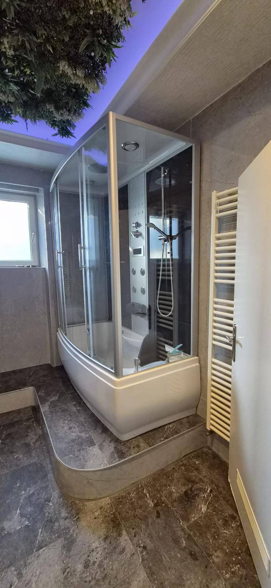 Modernes Badezimmer mit großer Duschkabine, dunklen Fliesen und Fenster.