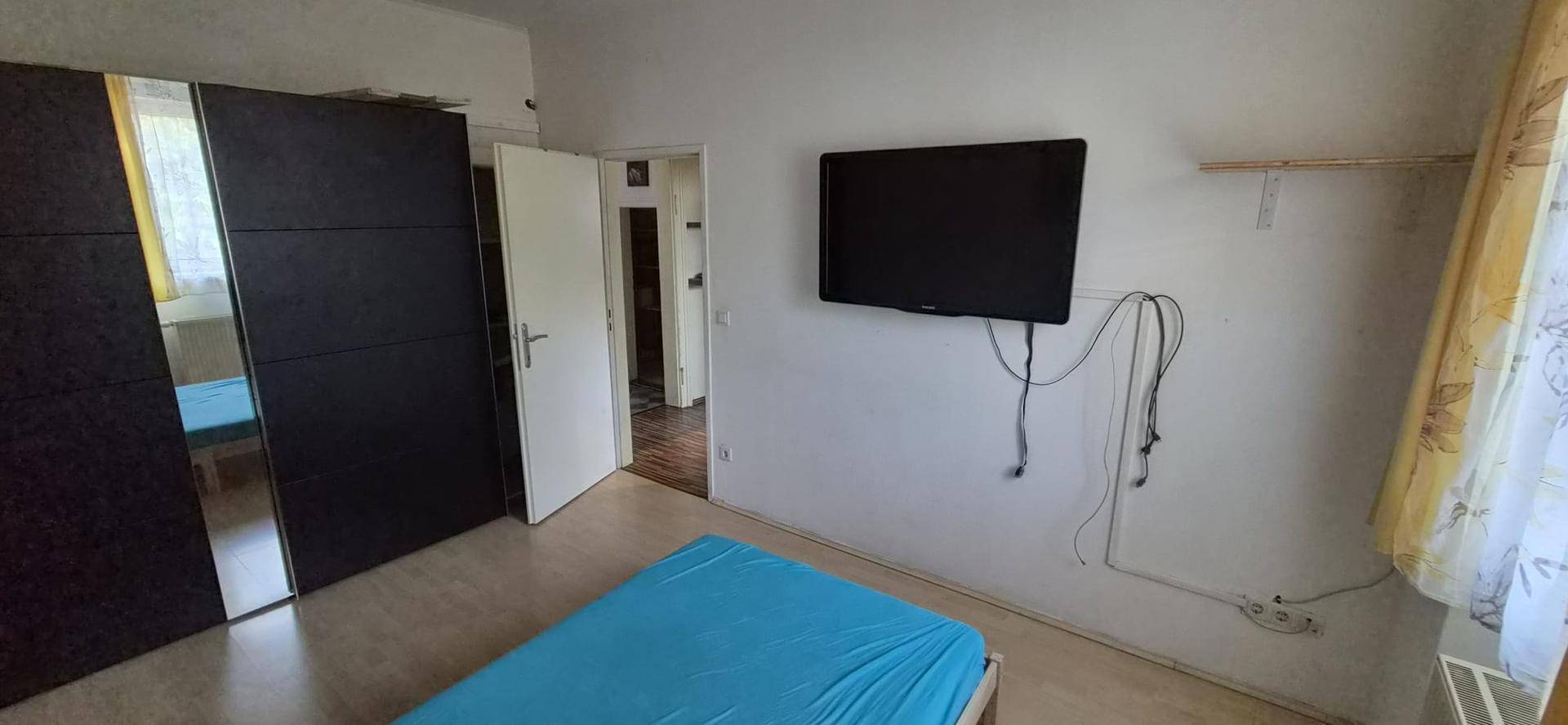 Schlafzimmer mit dunklem Kleiderschrank, hellem Boden und Wandmontage für Fernseher.