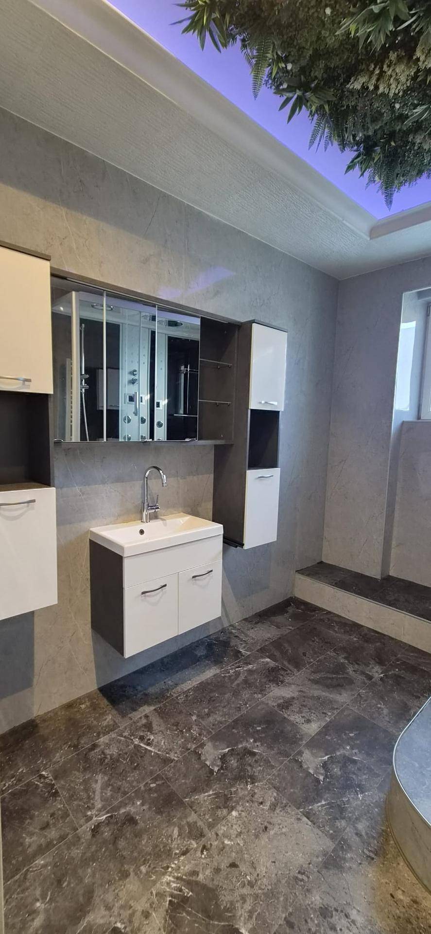 Badezimmer mit modernem Waschtisch, Spiegelschrank und dunklem Fliesenboden.