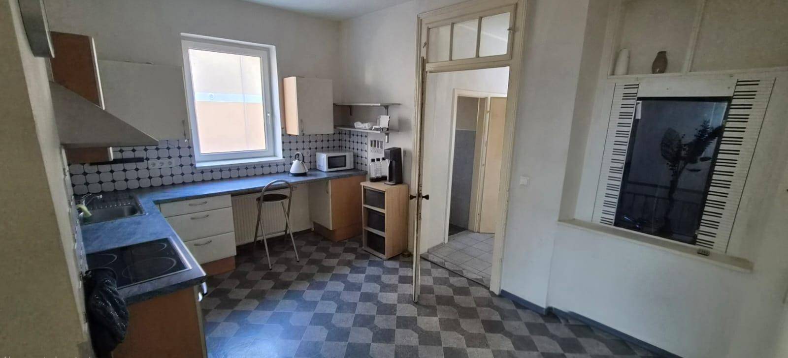 Ältere Küche mit kariertem Fliesenboden, Fenster und einfacher Einbauküche.