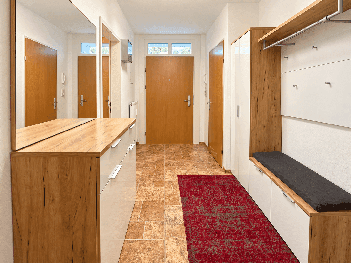 Heller Eingangsbereich mit Holzmöbeln, Fliesenboden und integrierter Garderobe.