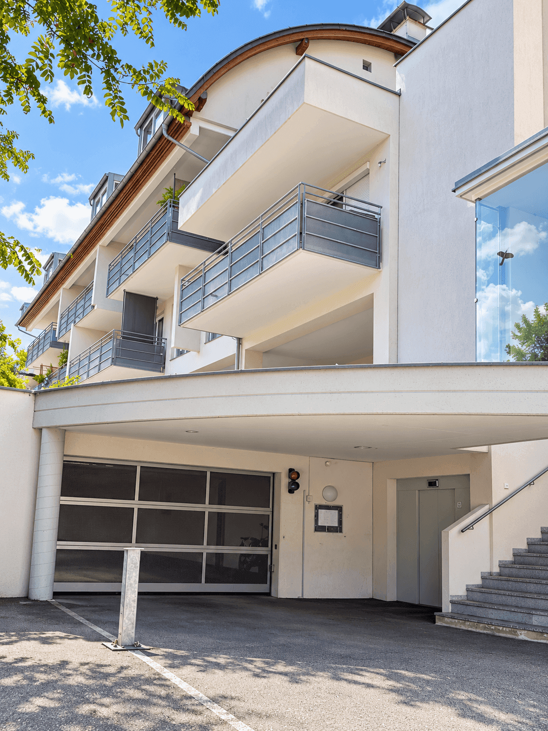 Moderne Gebäudefassade mit Balkonen, Tiefgaragenzufahrt und Aufzug im Freien.