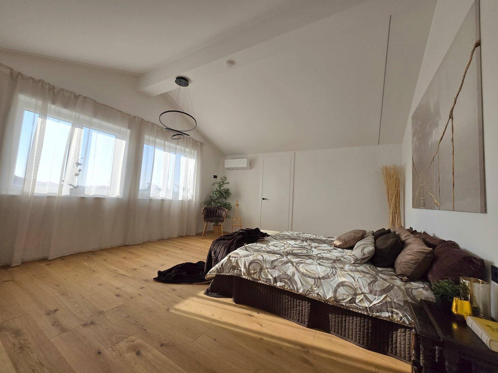 Geräumiges Schlafzimmer im Dachgeschoss mit Holzboden, großen Fenstern und Dachschräge.