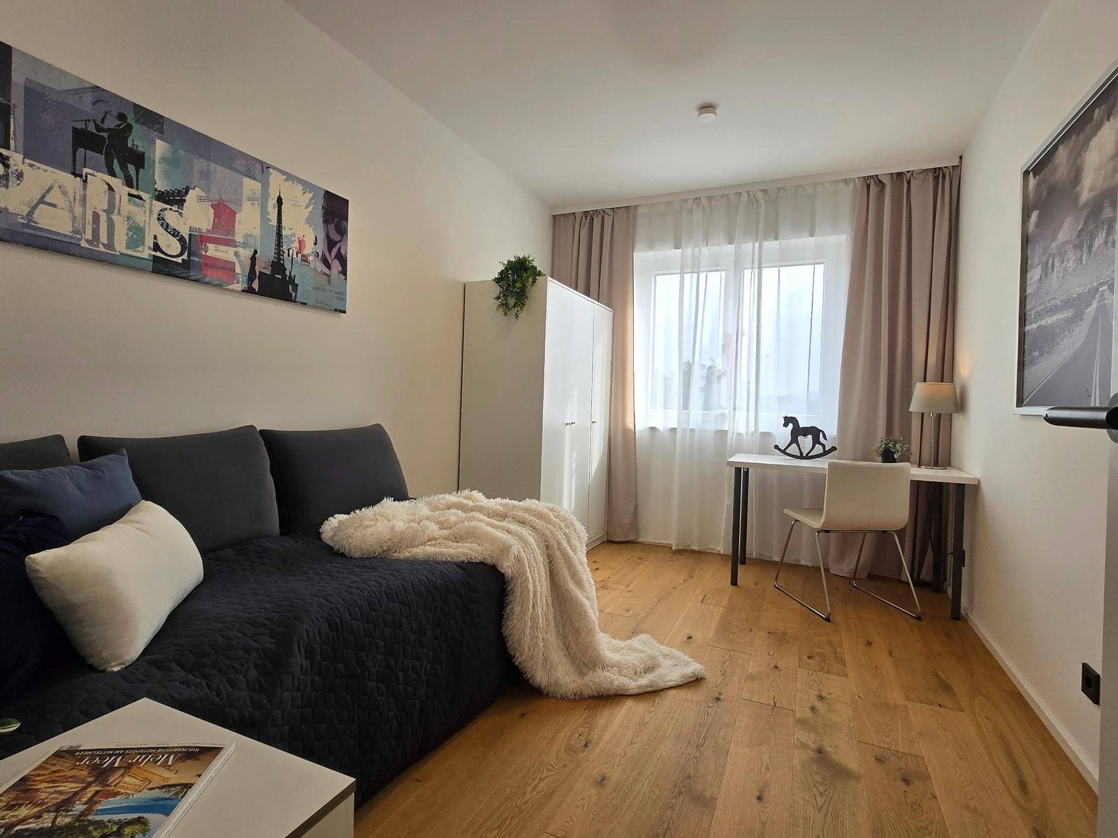 Helles Schlafzimmer mit Holzboden, Schreibtisch und Tagesbett, ideal als Kinder- oder Gästezimmer.