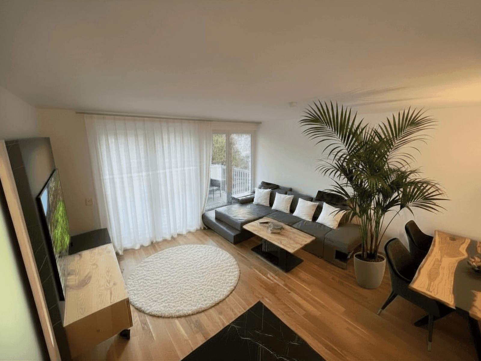 Heller Wohn- und Essbereich mit modernem Sofa, Holzboden und Zugang zu einem Balkon.