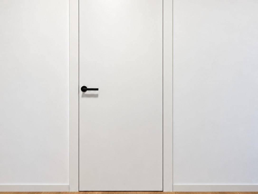 Moderne weiße Innentür mit schwarzem Griff, eingebettet in eine schlichte Wand.