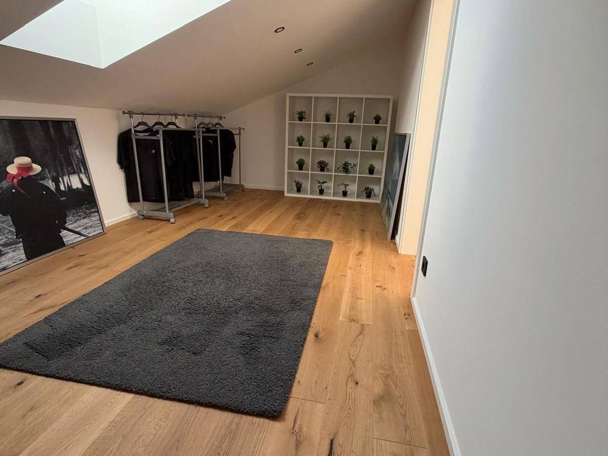 Geräumiger Raum im Dachgeschoss mit Holzboden, Dachschräge und offenem Kleiderständer.