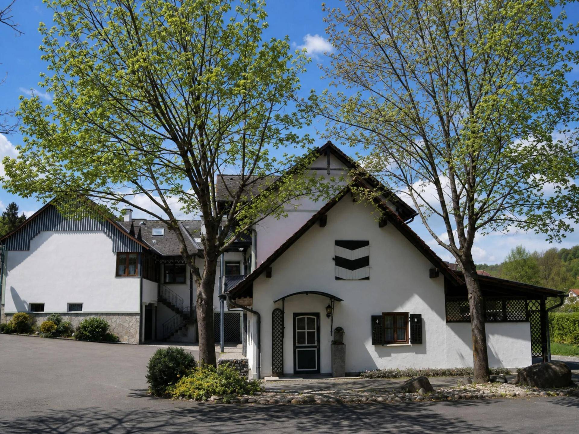 Eingangsbereich des Anwesens mit Bäumen und traditioneller Fassade unter blauem Himmel.