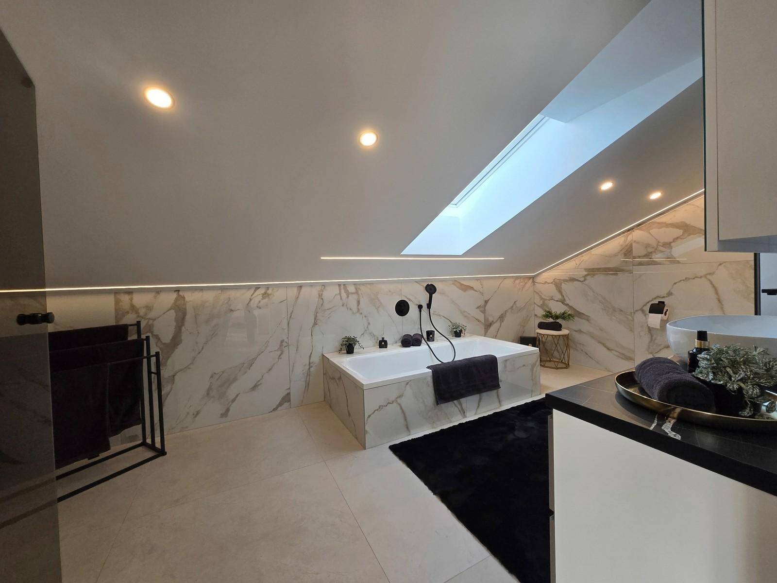 Luxuriöses Badezimmer im Dachgeschoss mit Badewanne, Marmorfliesen und Dachfenster.