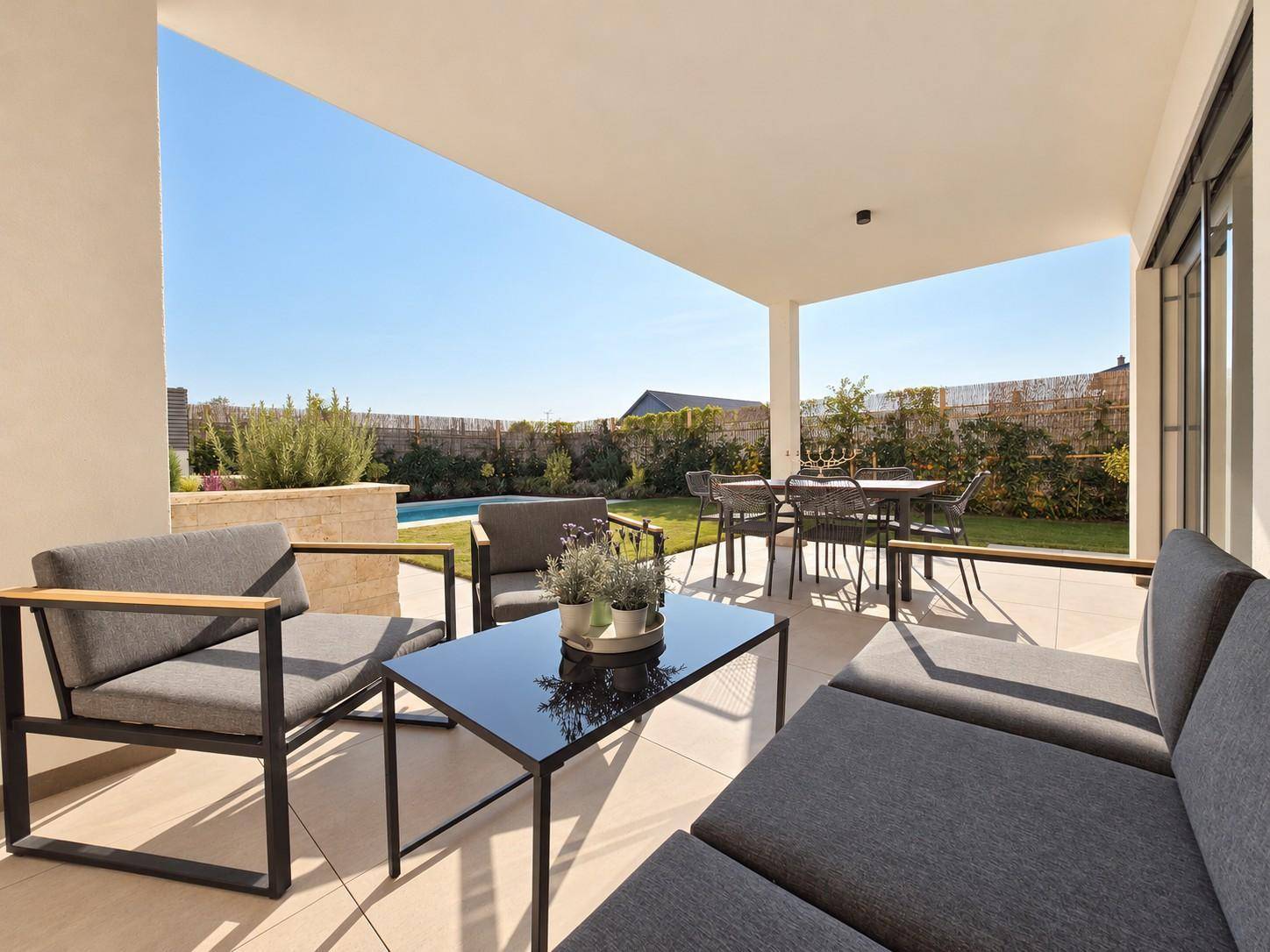 Überdachte Terrasse mit bequemen Lounge-Möbeln und Essbereich, direkt am Pool und Garten gelegen.