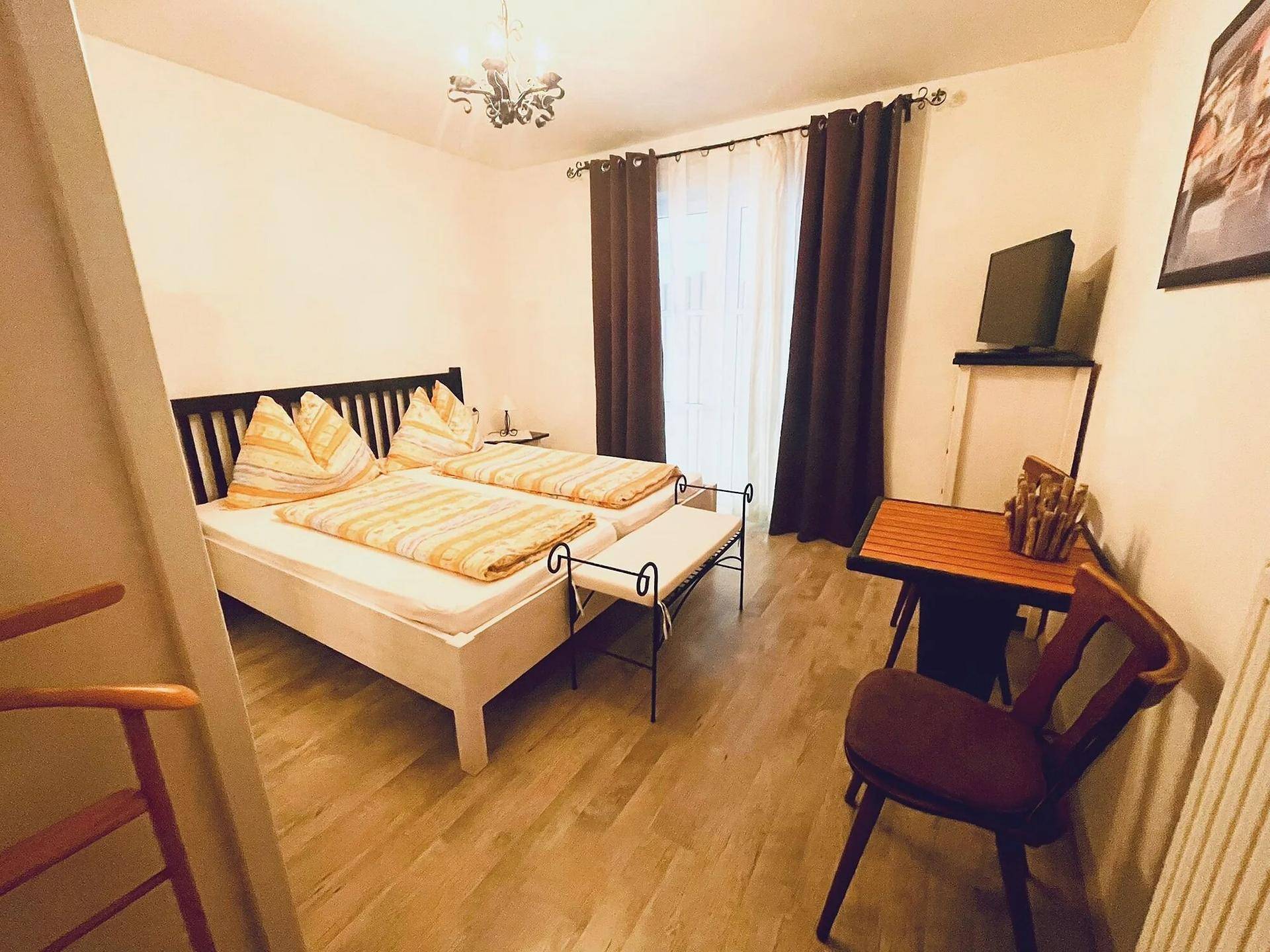 Helles Schlafzimmer mit zwei Einzelbetten, Holzmöbeln und einem Fenster mit dunklen Vorhängen.