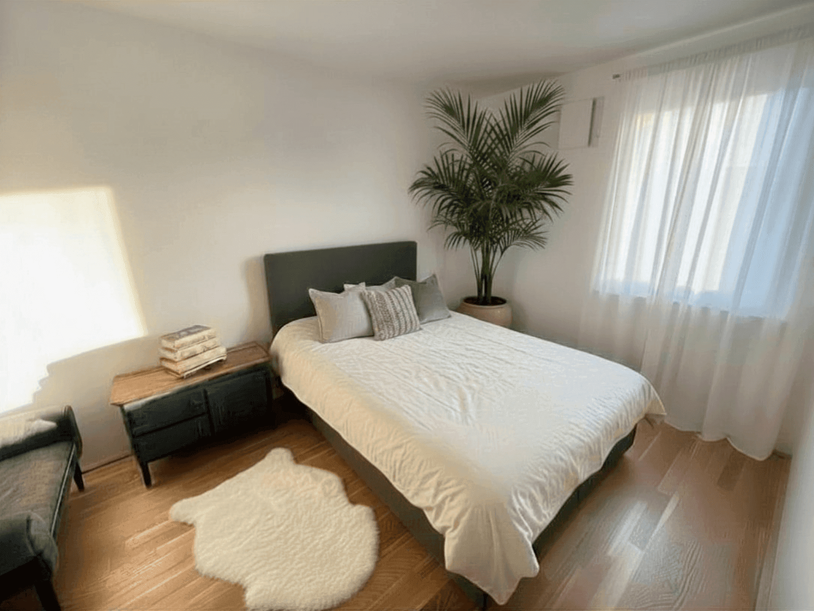 Helles Schlafzimmer mit Holzboden, großem Bett und einer Zimmerpflanze für eine gemütliche Atmosphäre.