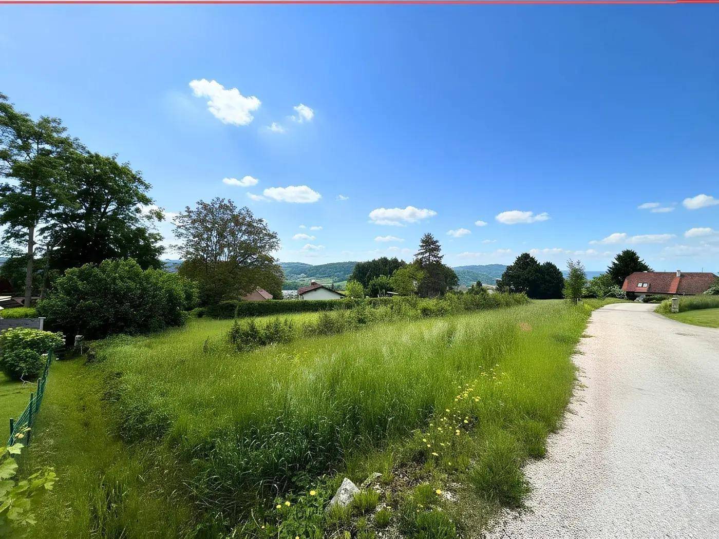 Grünes Grundstück mit einer unbefestigten Straße und Blick auf die umliegende Landschaft.