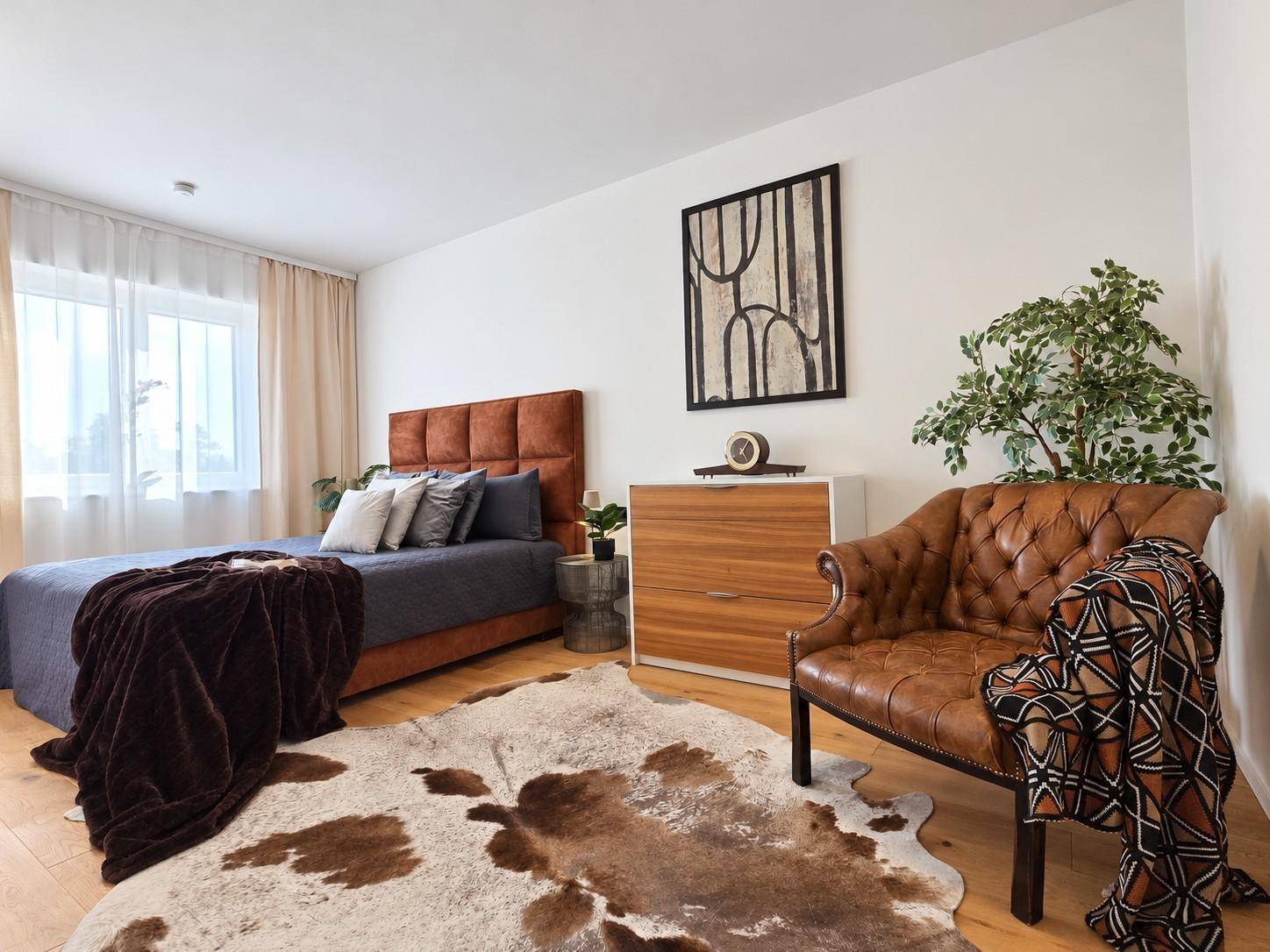 Gemütliches Schlafzimmer mit Holzboden, großem Bett und Ledersessel, hell und einladend gestaltet.