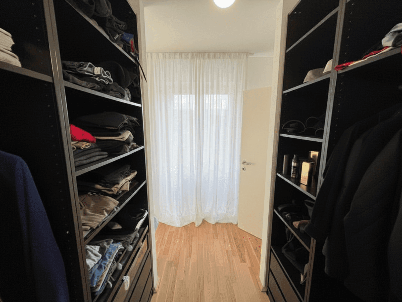 Geräumiger begehbarer Kleiderschrank mit viel Stauraum und natürlichem Lichteinfall durch das Fenster.