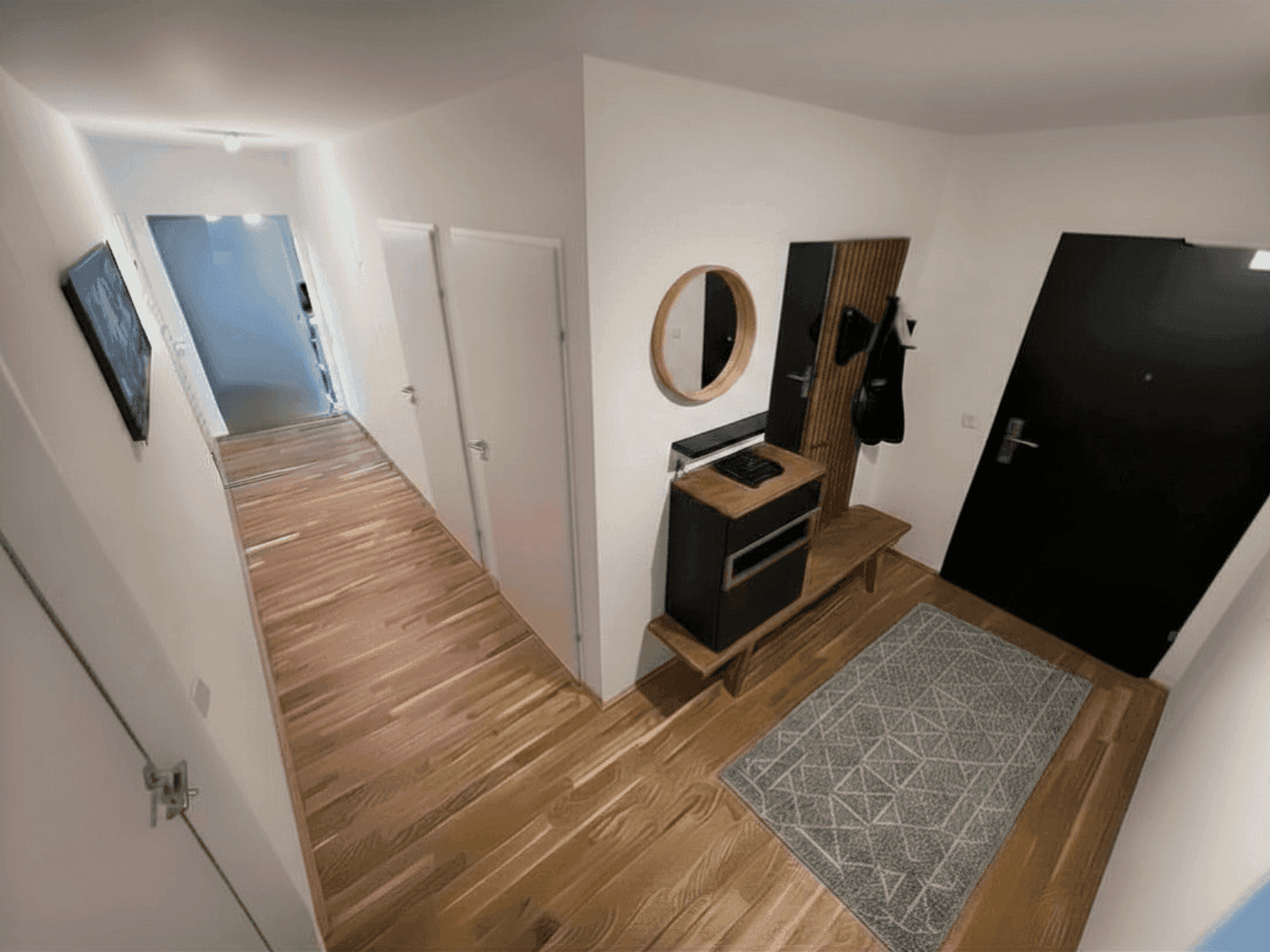 Heller Eingangsbereich mit Holzboden, Garderobe und Spiegel, der zu den weiteren Räumen führt.