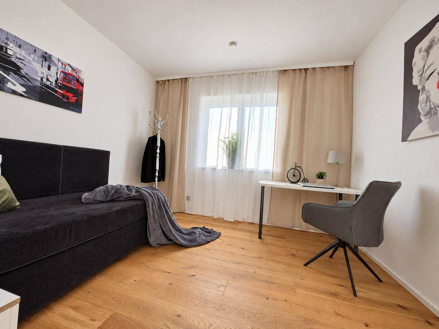 Schlafzimmer mit Holzboden, Tagesbett und Schreibtisch, hell und funktional eingerichtet.