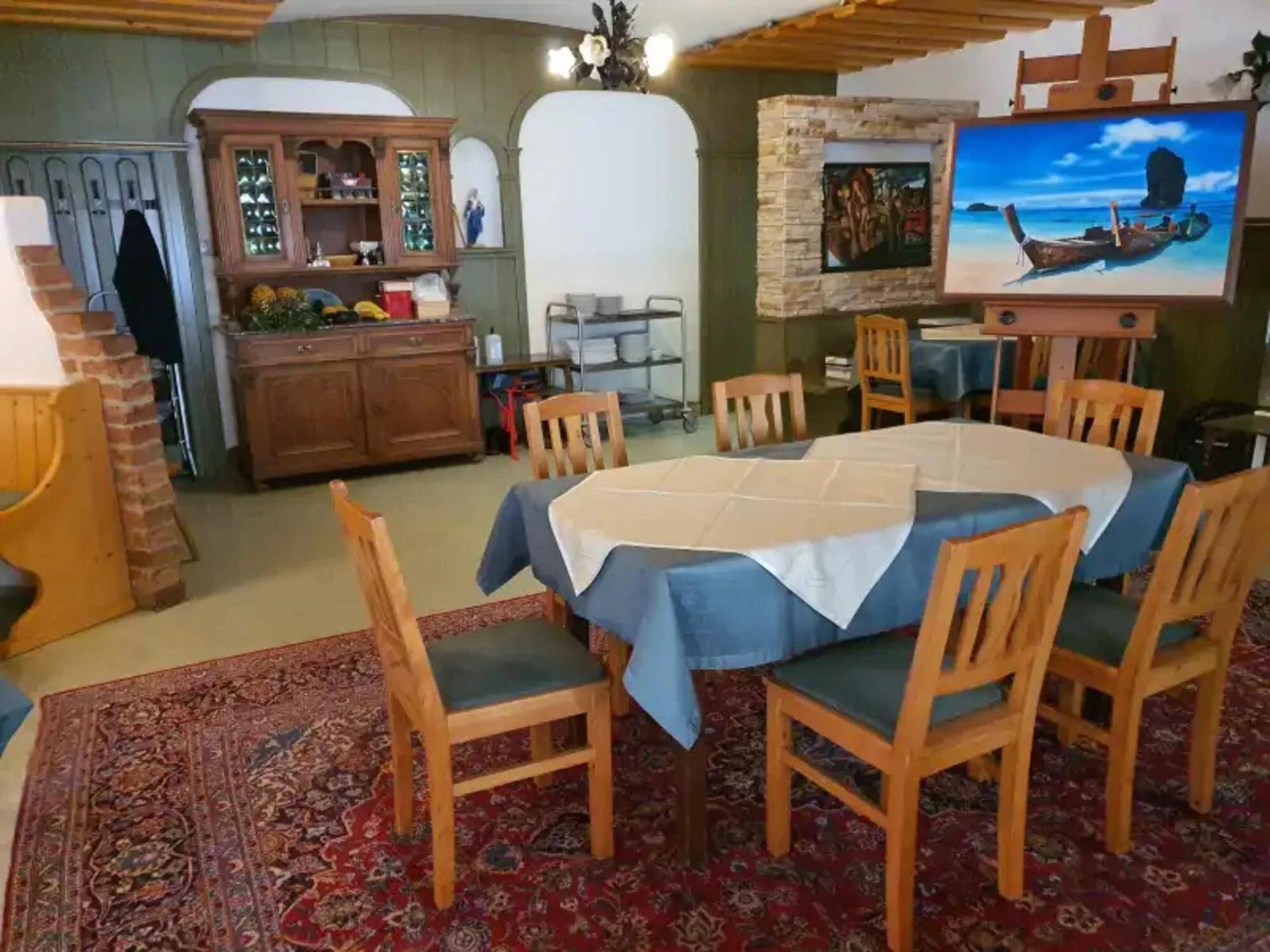 Traditioneller Speisesaal mit Holztischen, Stühlen, einem antiken Schrank und Kunstwerken.