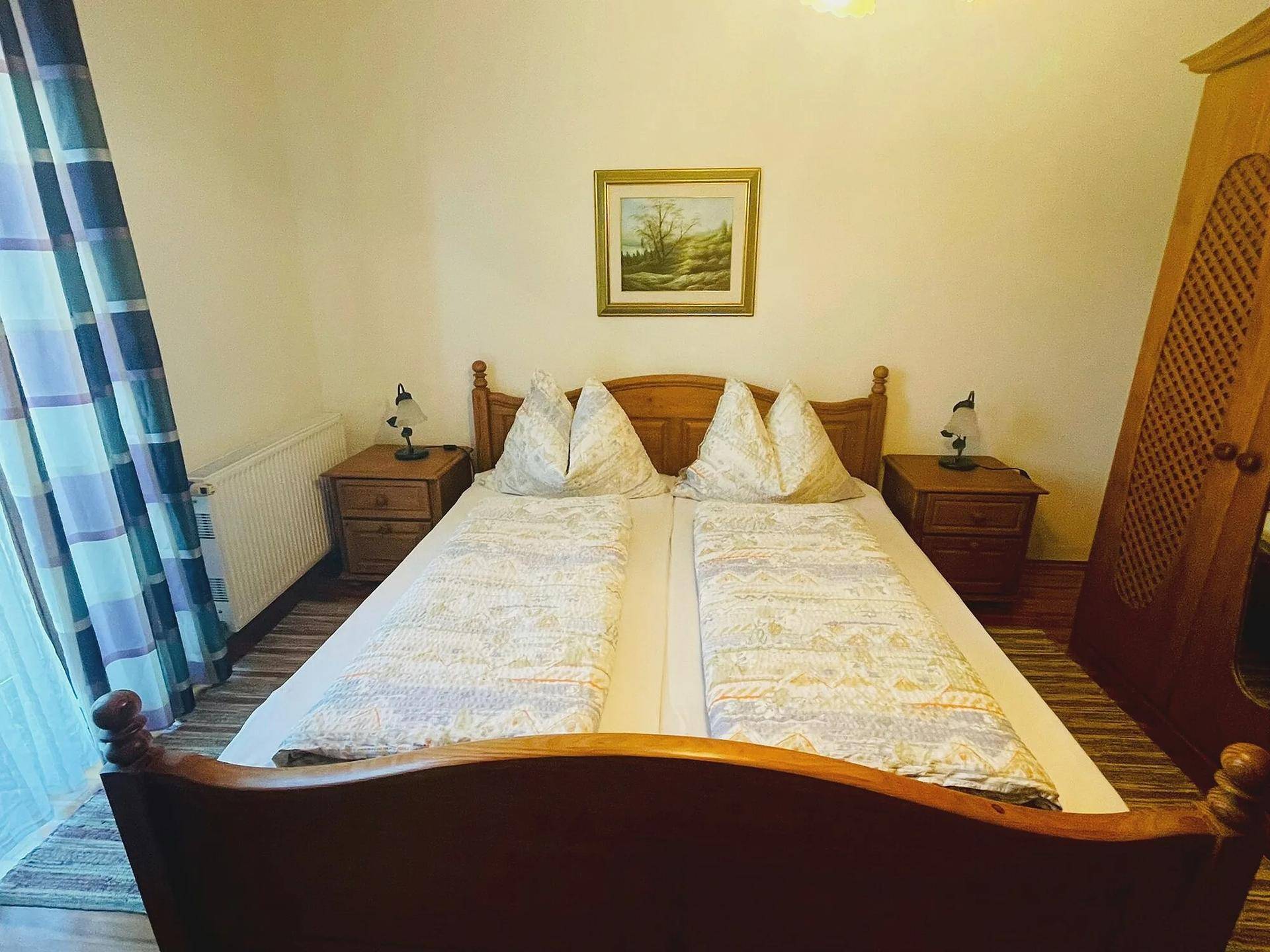 Gemütliches Schlafzimmer mit zwei Einzelbetten, Holzmöbeln und einem Fenster mit Vorhängen.