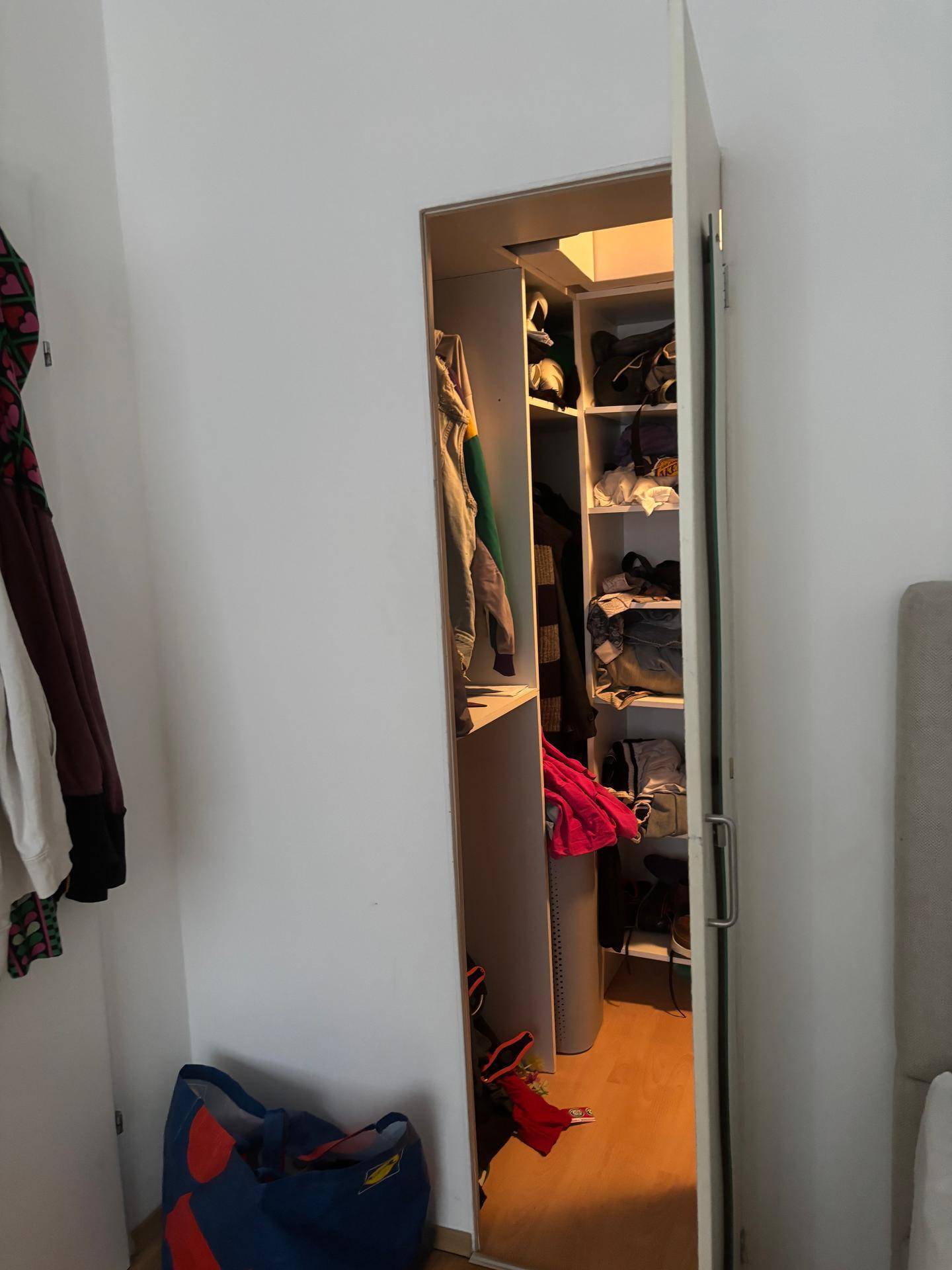 Offener Kleiderschrank mit Regalen und Kleiderstange in einem Schlafzimmer.