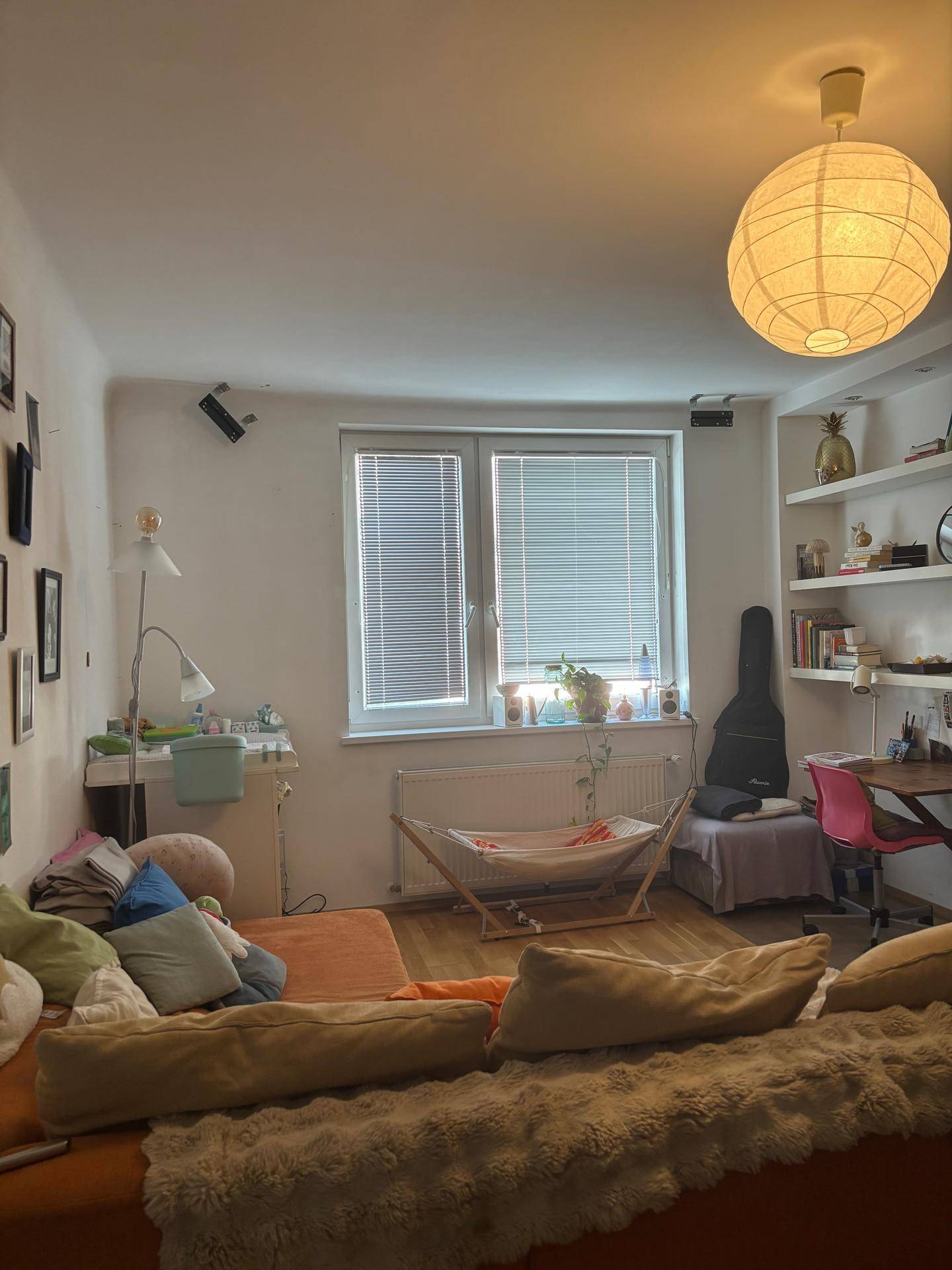 Wohnzimmer mit hellem Holzfußboden, Fenster mit Jalousien und einem gemütlichen Sofa.