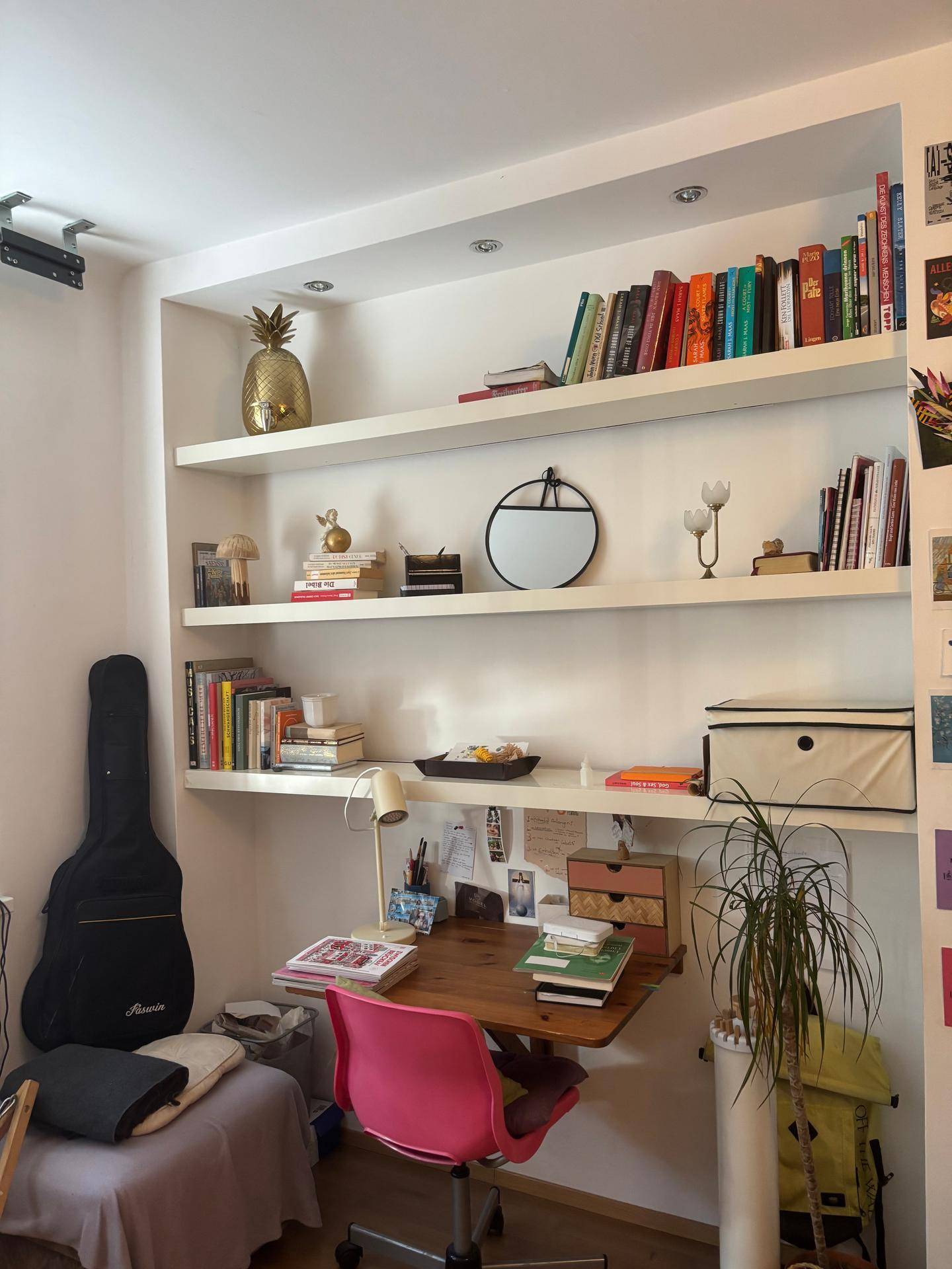 Arbeitsplatz mit Schreibtisch, pinkem Stuhl und integrierten Wandregalen mit Büchern.