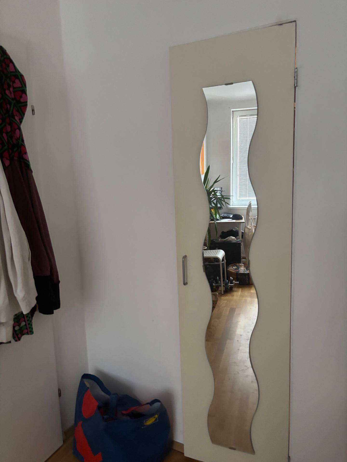 Kleiderschranktür mit einem wellenförmigen Spiegel, der den Raum reflektiert.