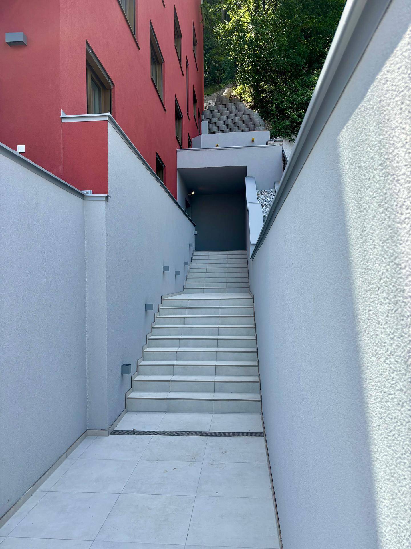 Moderner Außentreppenaufgang zwischen Gebäudeteilen mit roter Fassade und hellen Wänden.