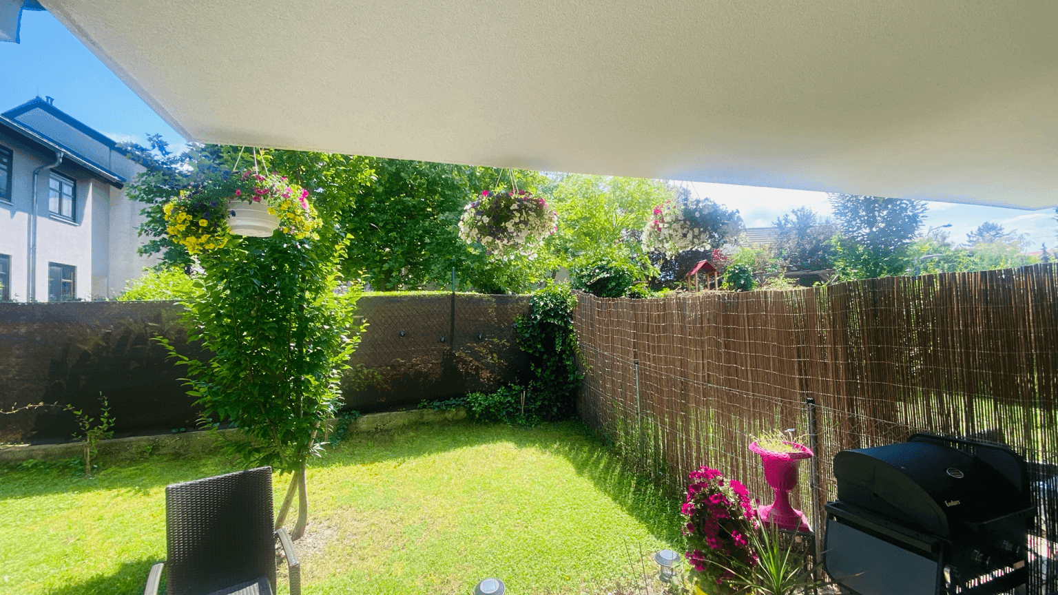 Gepflegter Garten mit Rasenfläche, Grillbereich und schattenspendender Überdachung für entspannte Stunden.