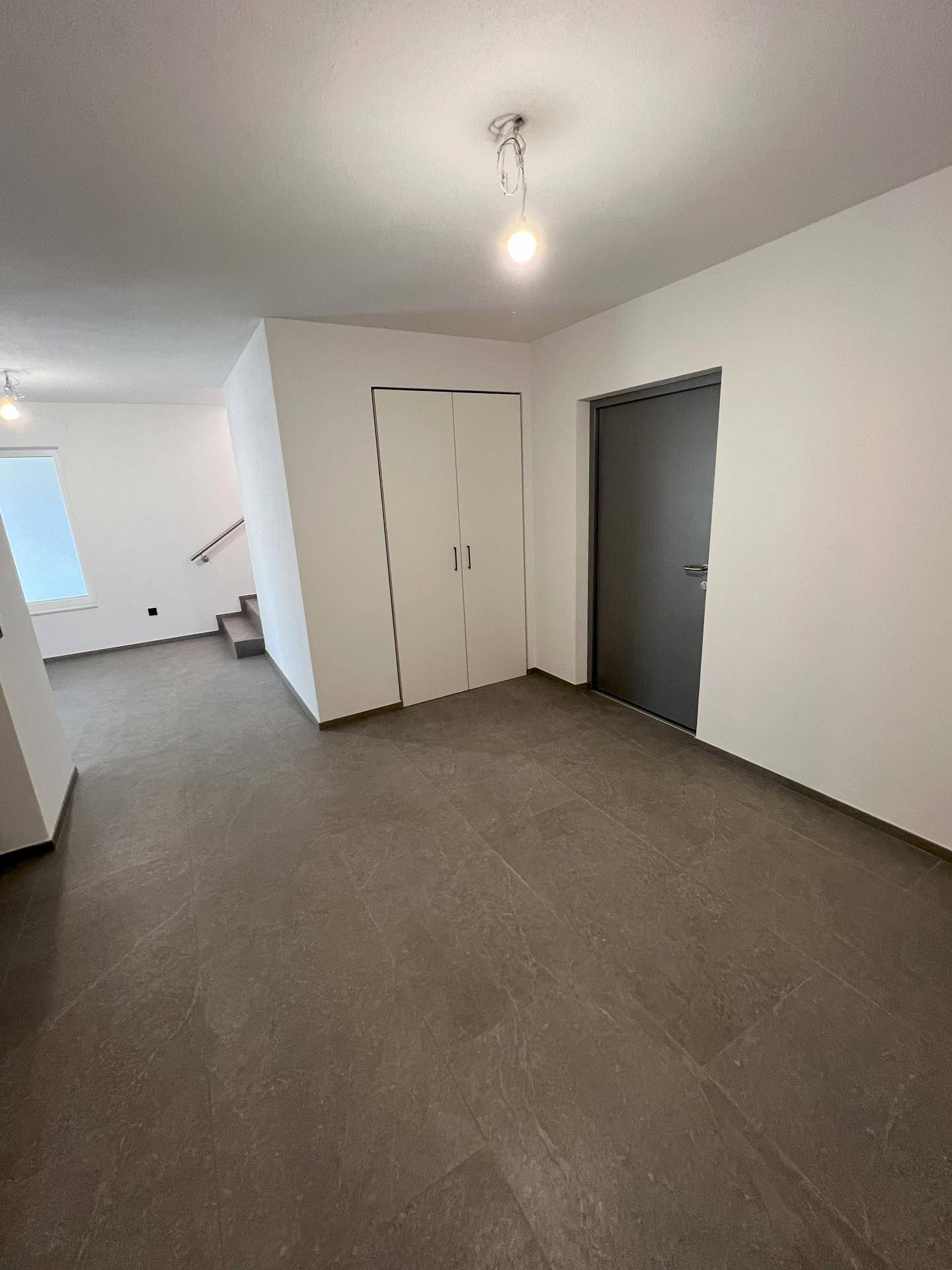 Geräumiger Flur mit Einbauschränken, dunkler Tür und modernem Fliesenboden.