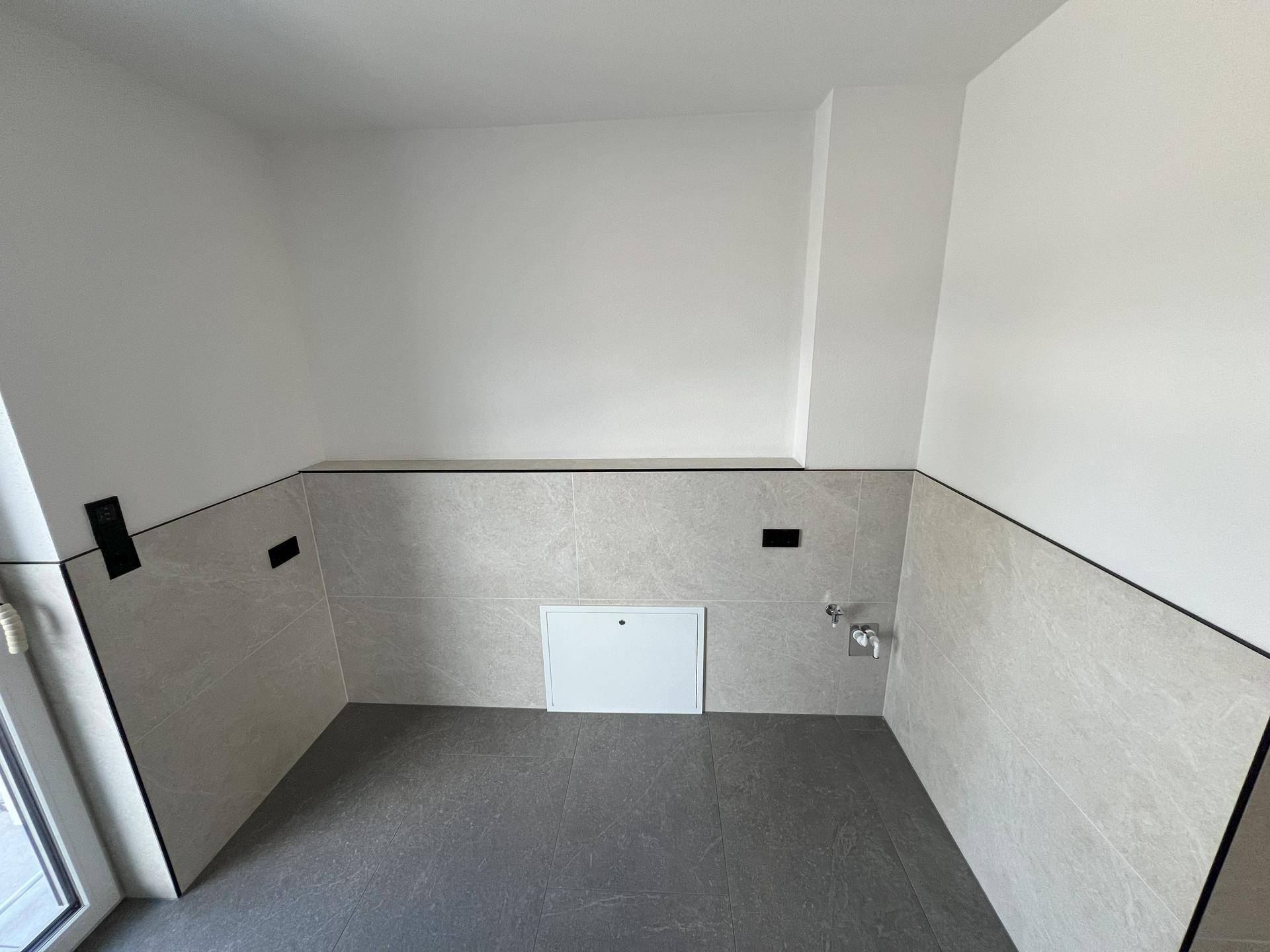 Praktischer Hauswirtschaftsraum mit Fliesenboden, halbhohen Wandfliesen und Anschlüssen.