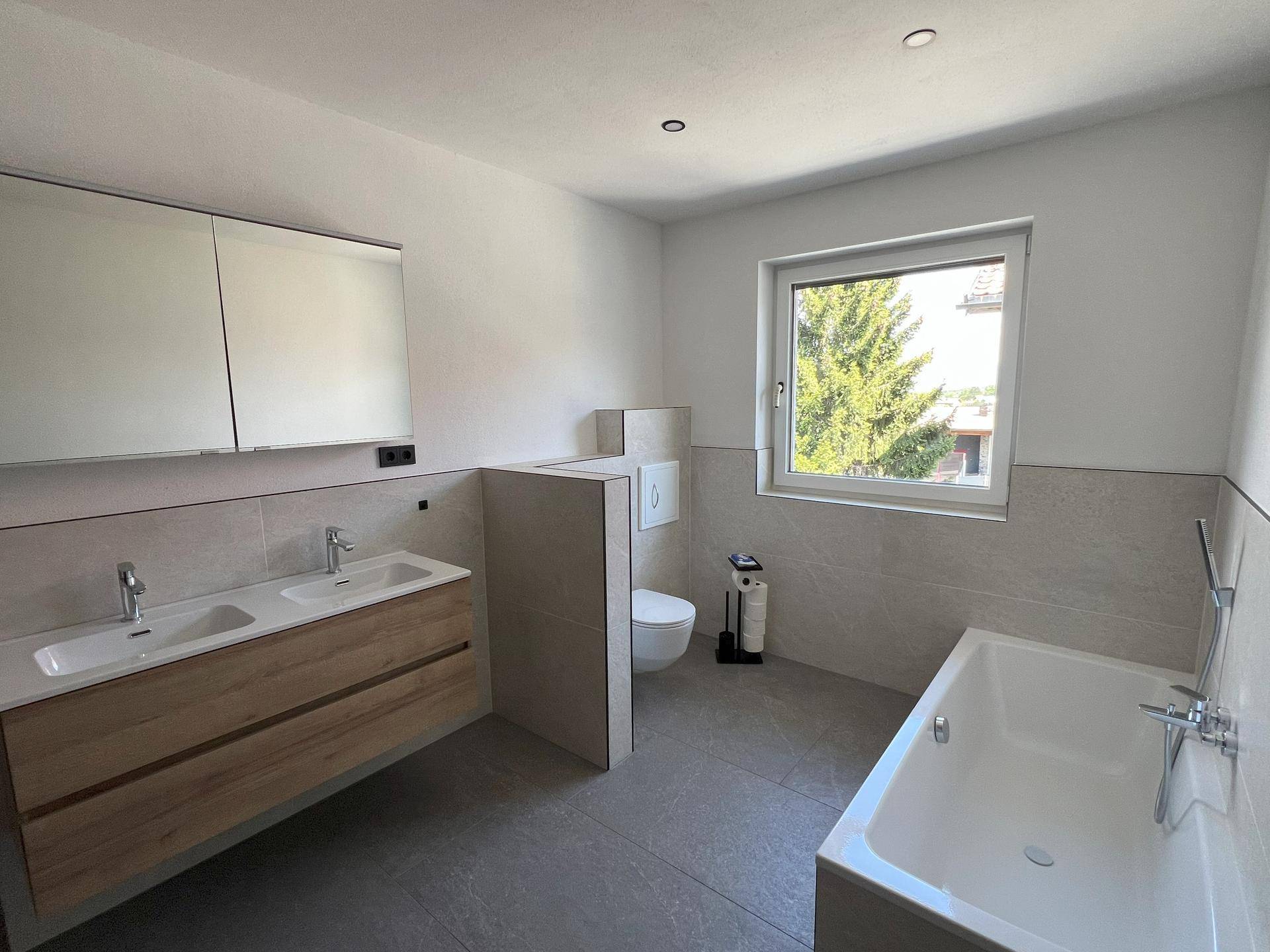 Geräumiges Badezimmer mit Doppelwaschbecken, Badewanne, Toilette und Fenster für Tageslicht.