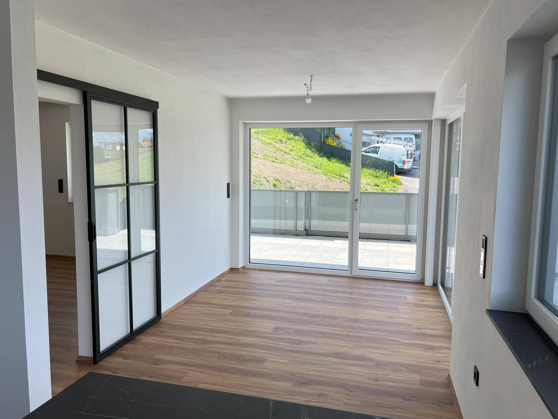 Heller Wohnbereich mit Laminatboden, Schiebetür und Zugang zu einer Außenterrasse.