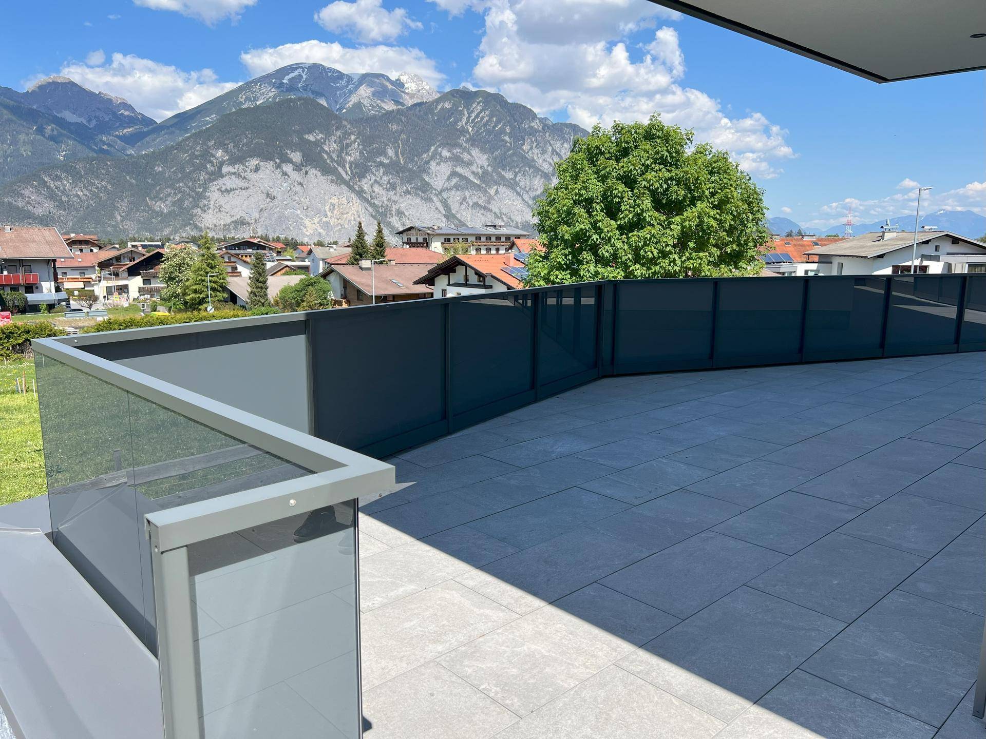 Geräumige, geflieste Terrasse mit Glasgeländer und weitem Blick auf die Berge und das Tal.
