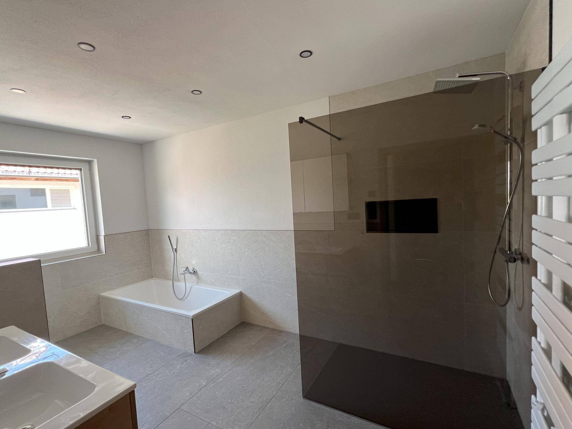 Modernes Badezimmer mit großer begehbarer Dusche, Badewanne und integrierten Deckenleuchten.