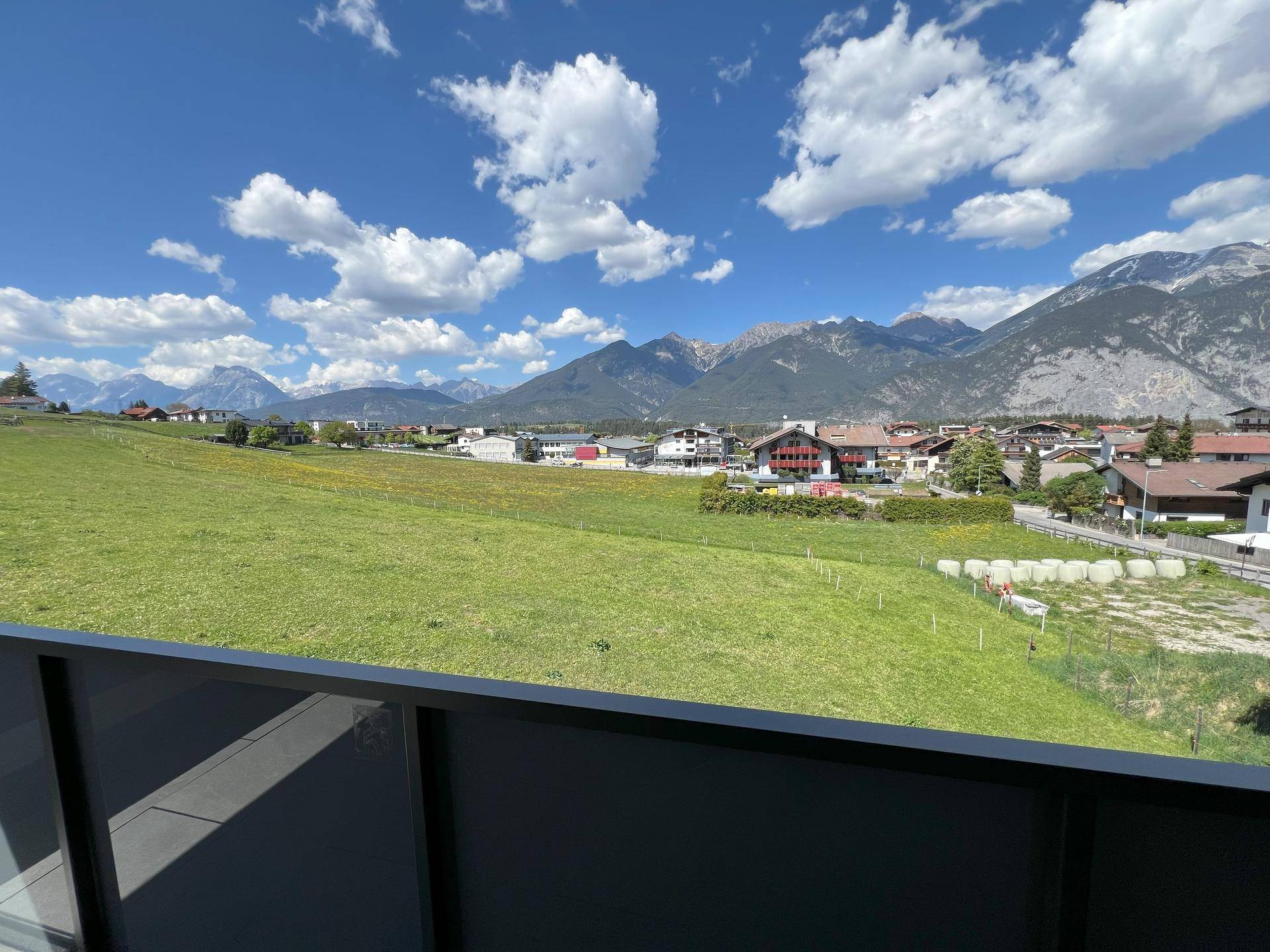 Panoramablick auf die umliegende Berglandschaft und grüne Wiesen unter blauem Himmel.