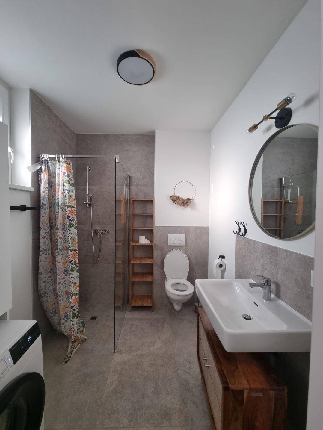 Modernes Badezimmer mit begehbarer Dusche, Waschbecken auf Holzunterschrank und Waschmaschine.