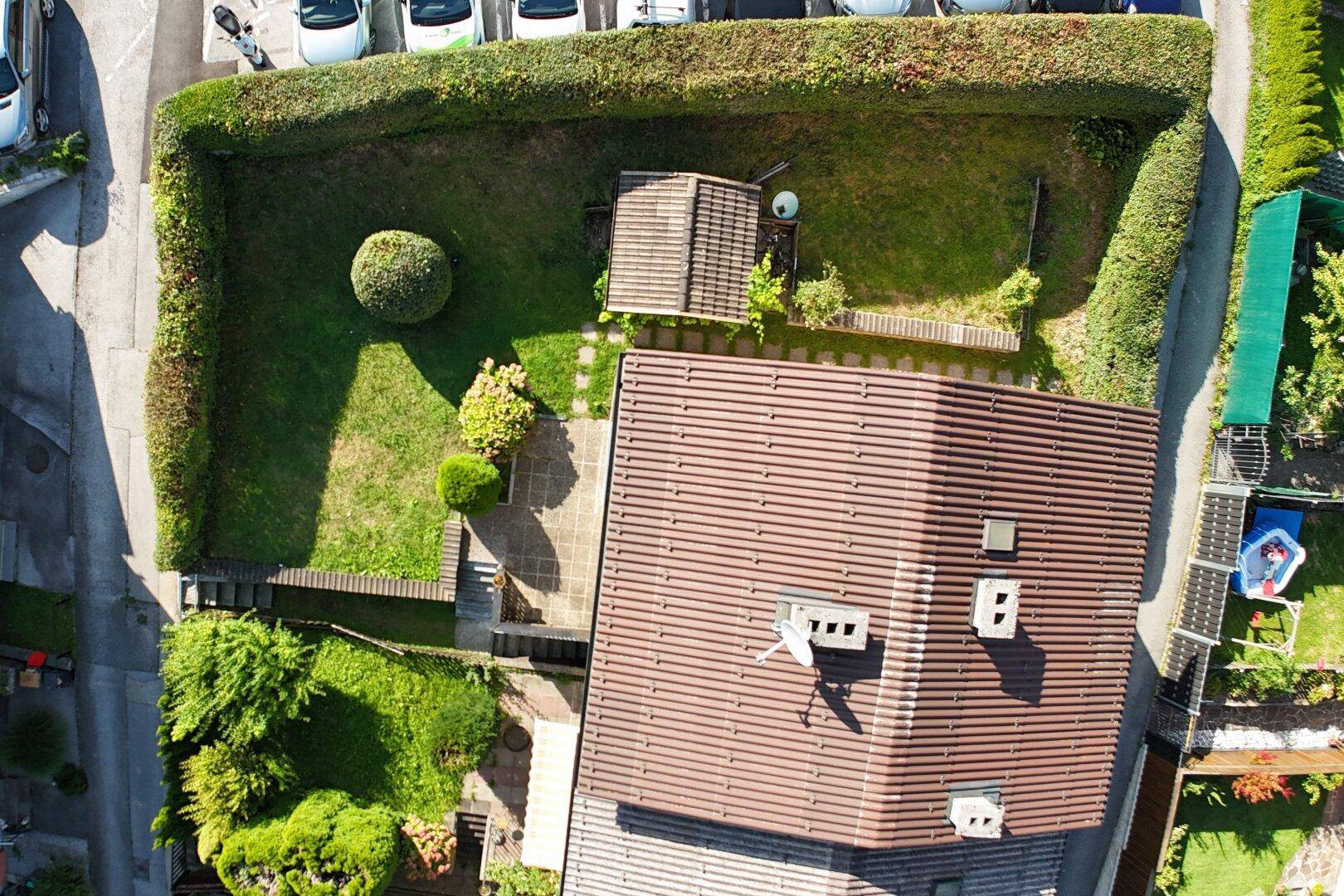 Luftaufnahme eines Wohnhauses mit gepflegtem Garten, Hecken und einem kleinen Schuppen.