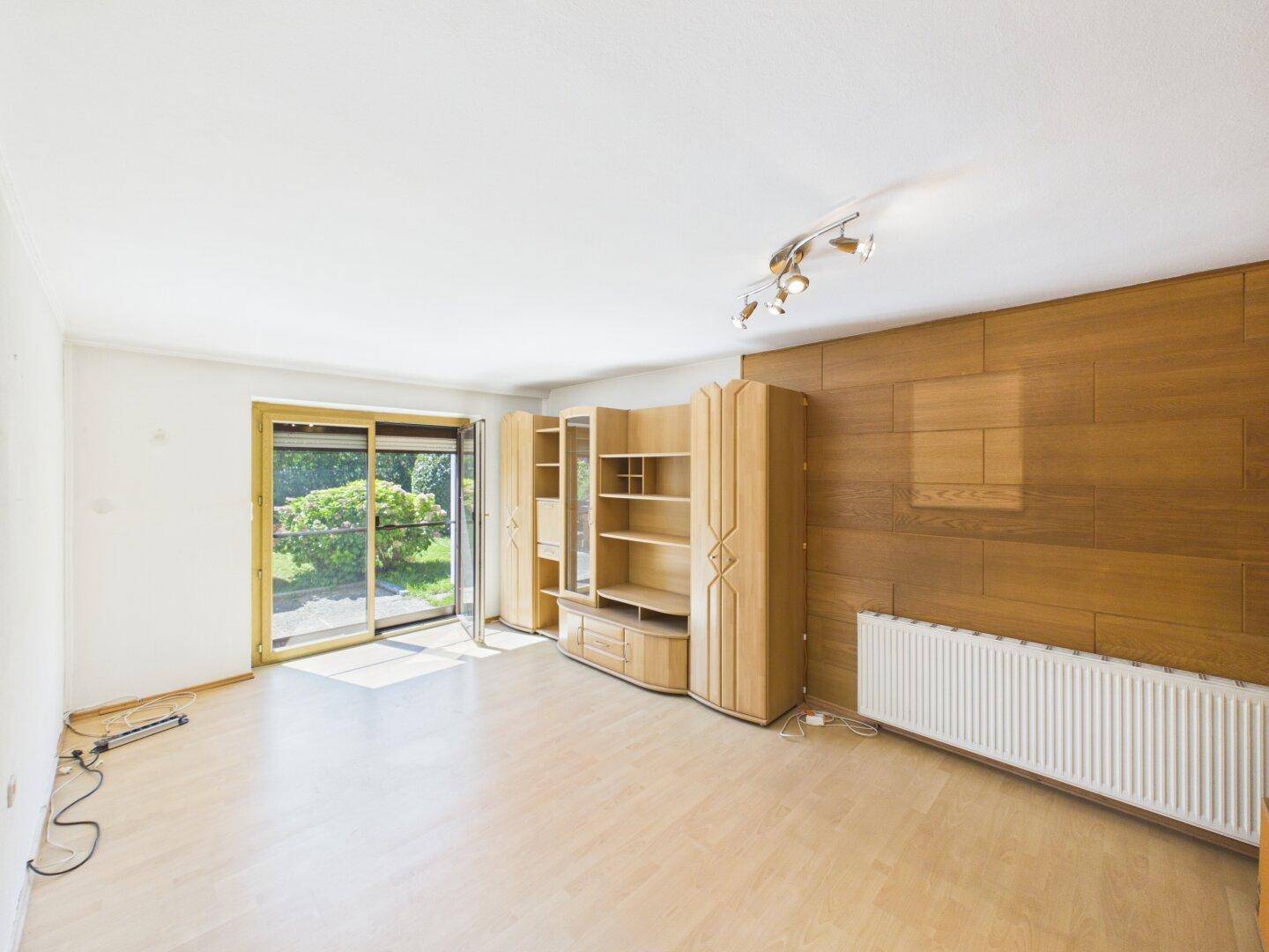 Helles Wohnzimmer mit hellem Laminatboden, Holzwandverkleidung und Zugang zum Garten.