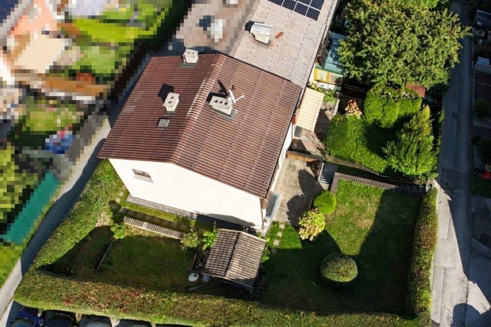 Luftaufnahme eines Wohnhauses mit Garten, Terrasse und umgebender Hecke.