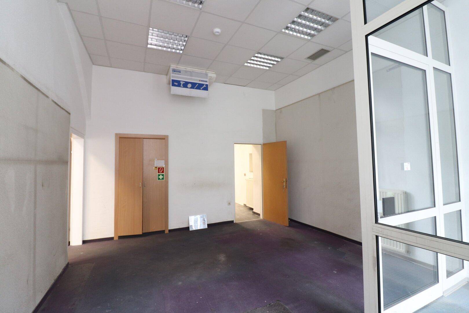 Leerer Gewerberaum mit lila Teppichboden, abgehängter Decke und großen Fenstern, bereit zur Nutzung.