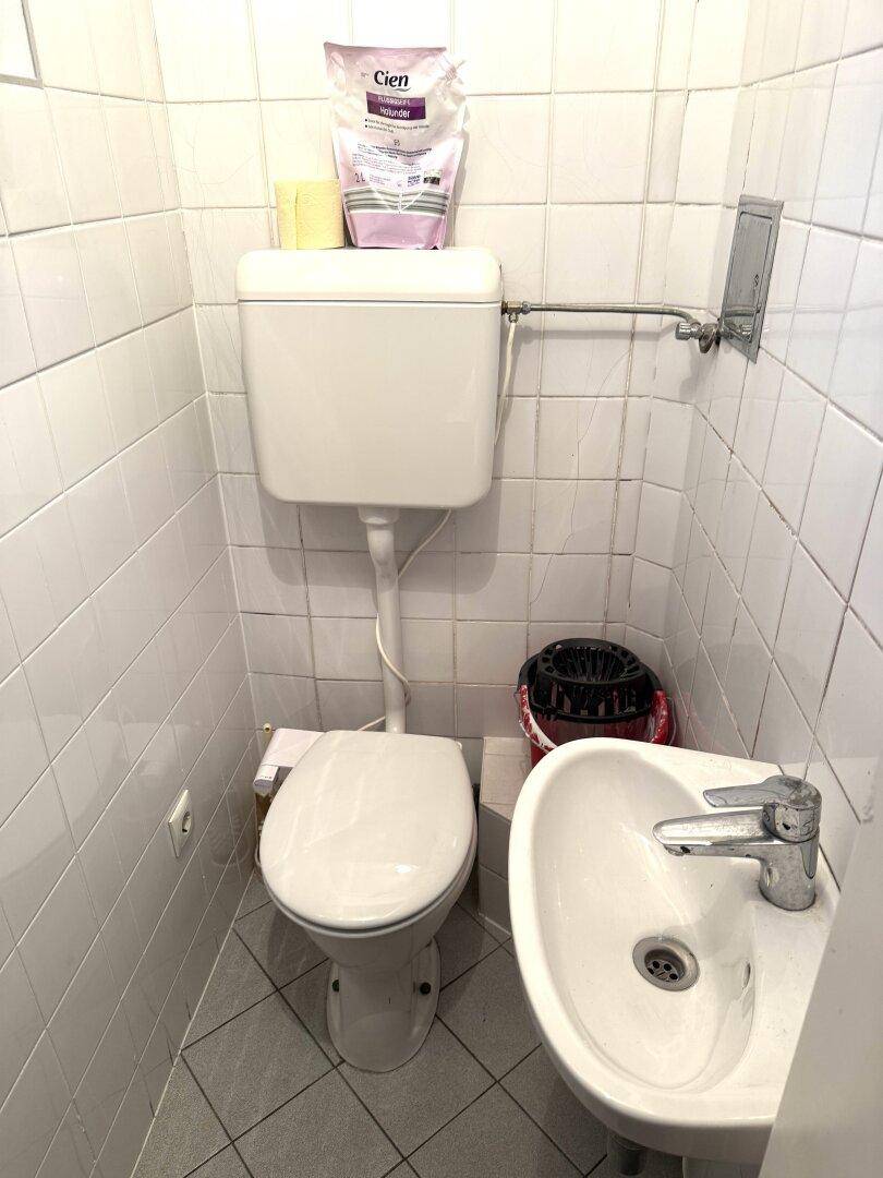 Kleiner Toilettenraum mit weißen Fliesen, WC und Handwaschbecken.