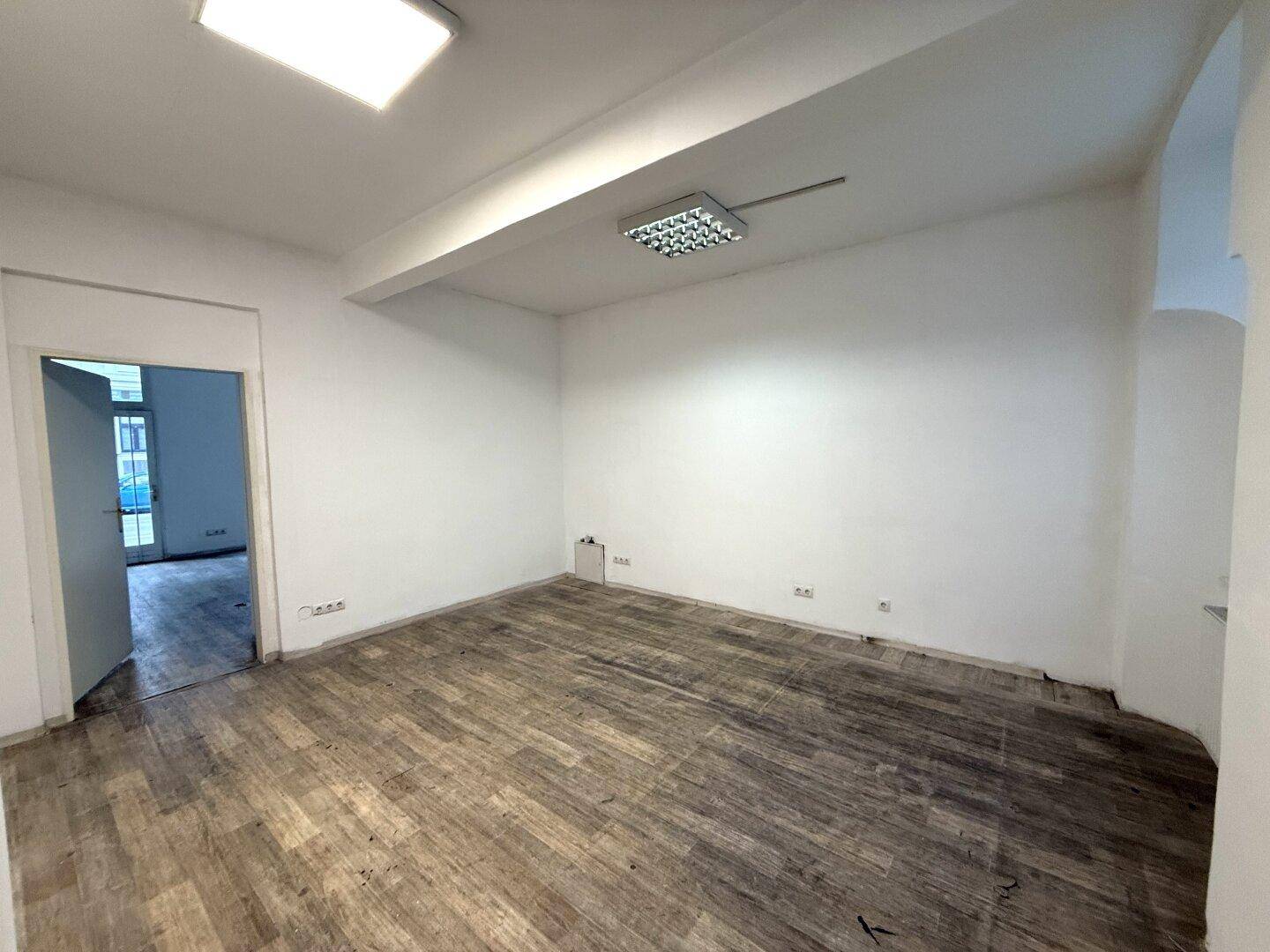 Geräumiger, leerer Büroraum mit Holzboden, weißen Wänden und moderner Deckenbeleuchtung.