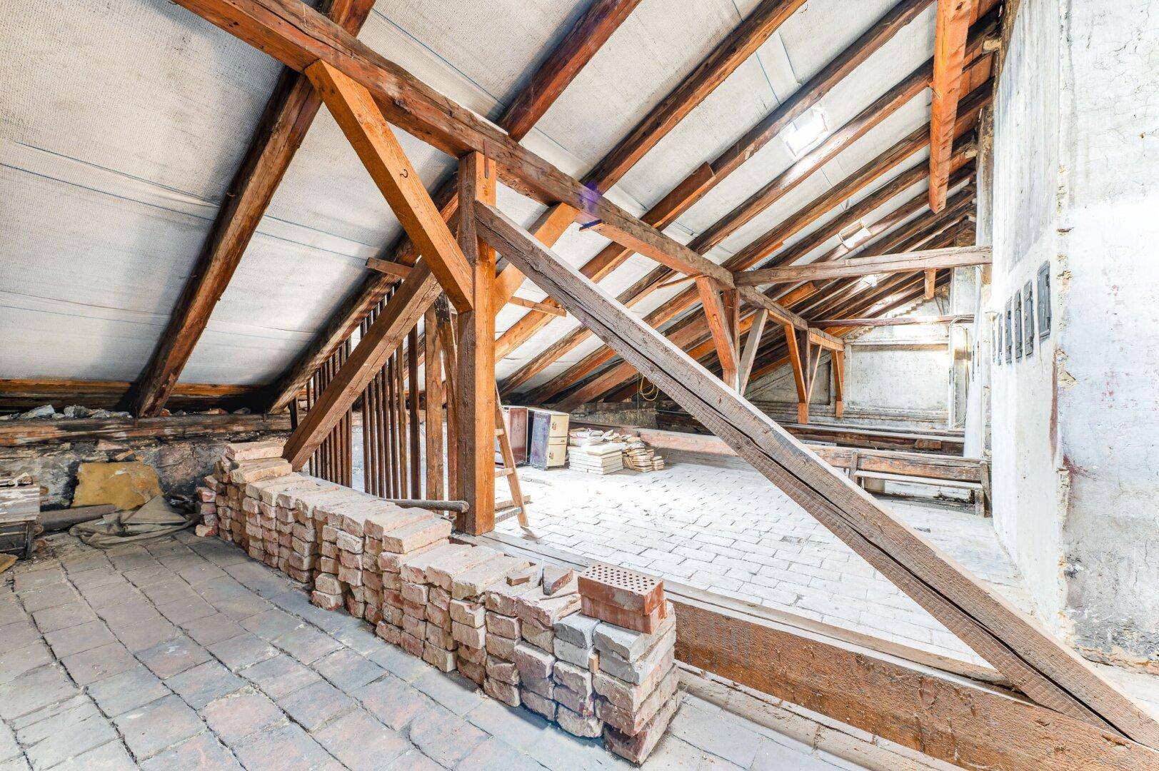 Geräumiger Dachboden mit sichtbaren Holzbalken und Ziegelboden, ideal für einen Ausbau.