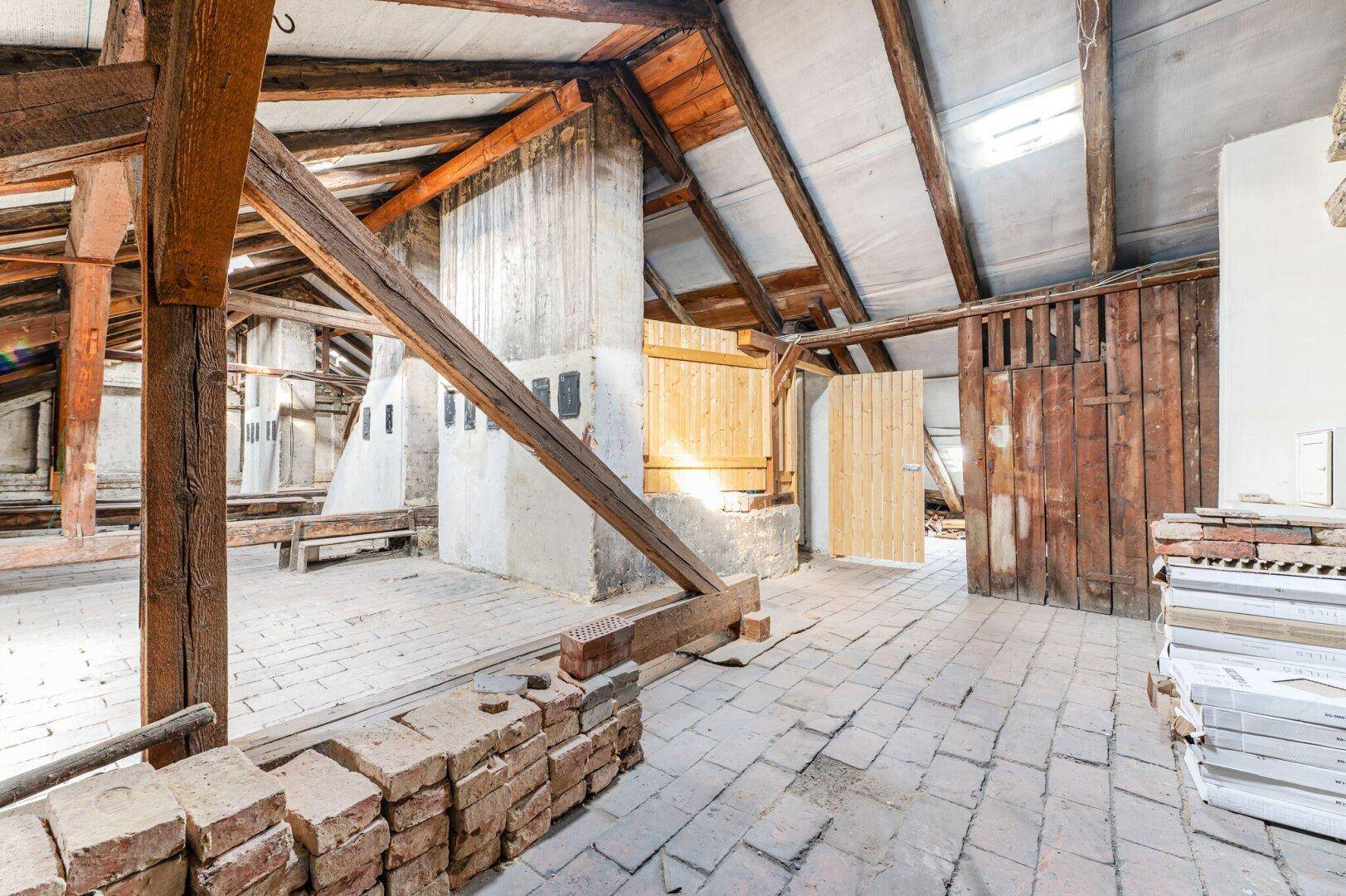 Dachboden mit rustikalen Holzbalken, Ziegelboden und alten Holztüren, bereit zur Renovierung.