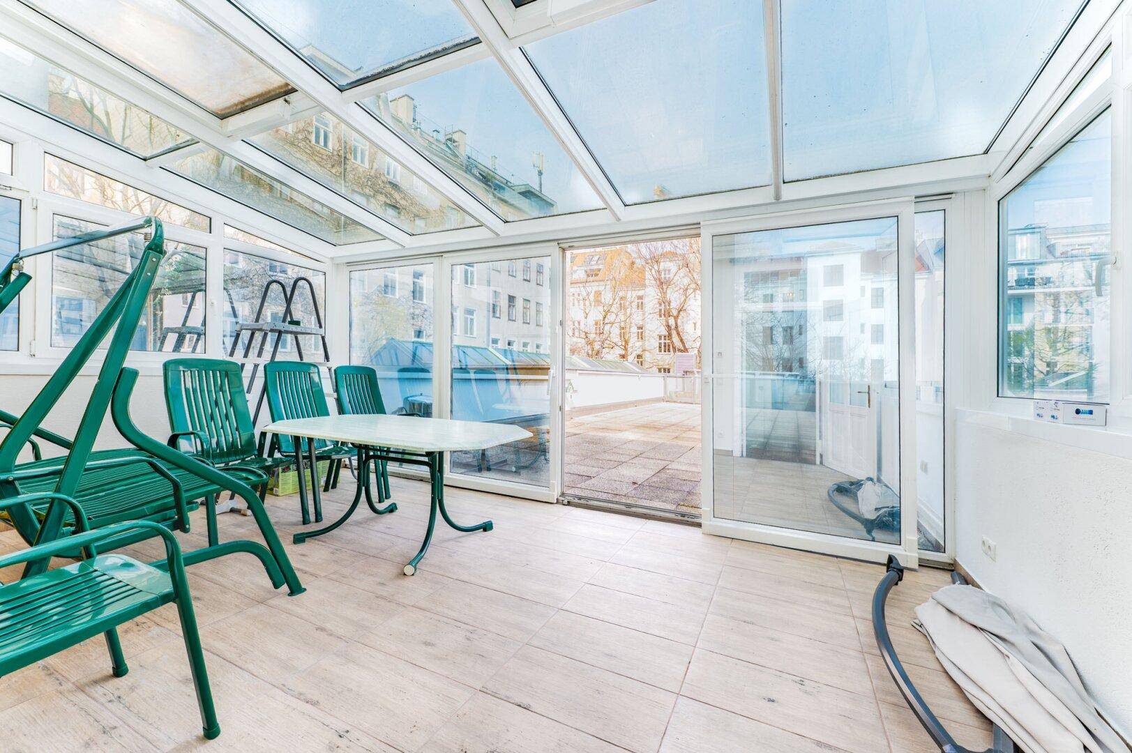 Heller Wintergarten mit Glasdach, Gartenmöbeln und direktem Zugang zu einer Terrasse.